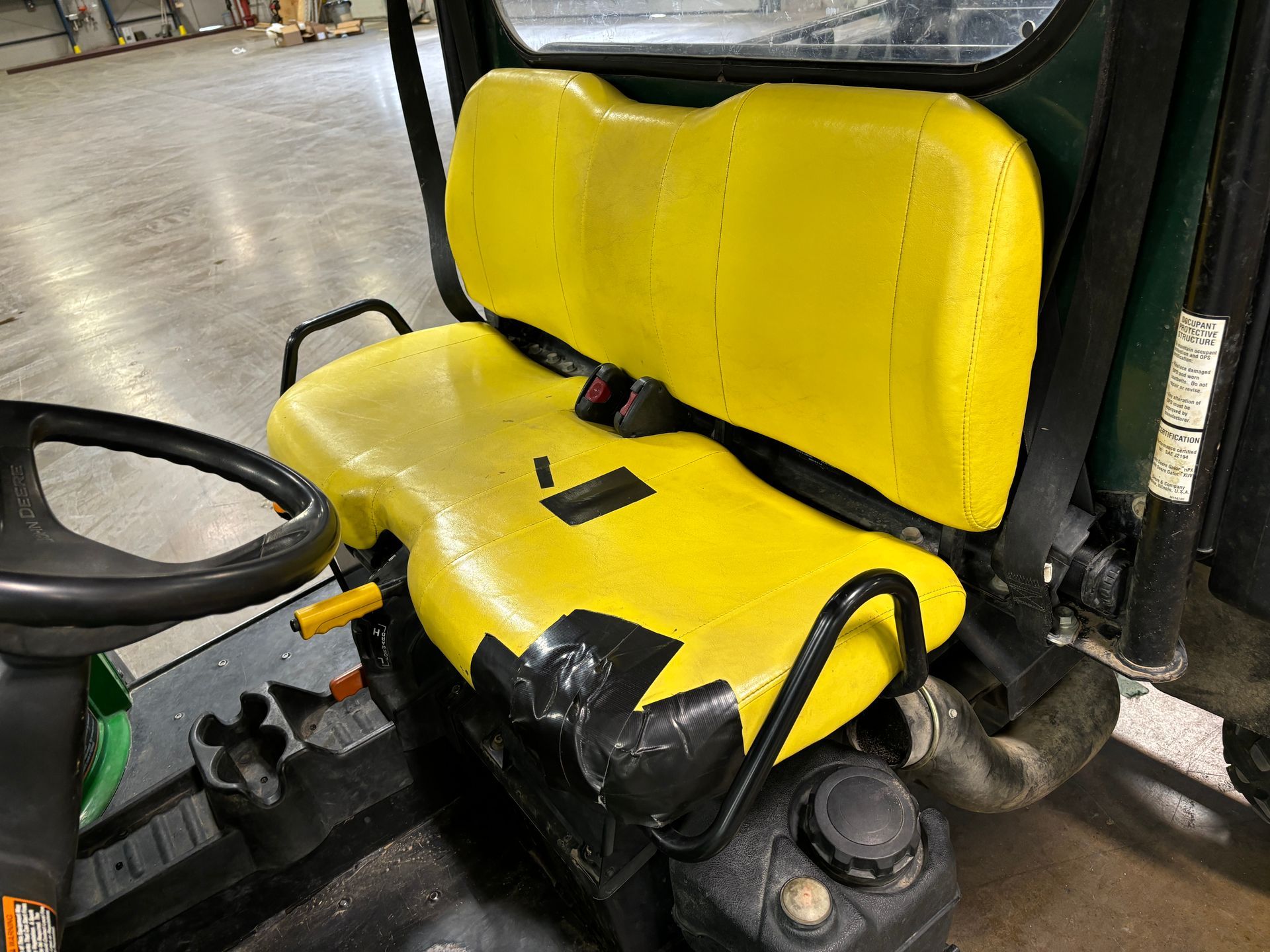 Yellow forklift seat with black duct tape, steering wheel, industrial setting.