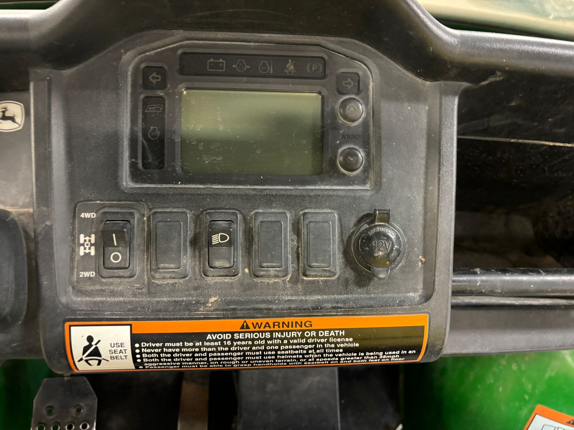 Dashboard of a John Deere Gator utility vehicle with a display screen, switches, and a 12V outlet.