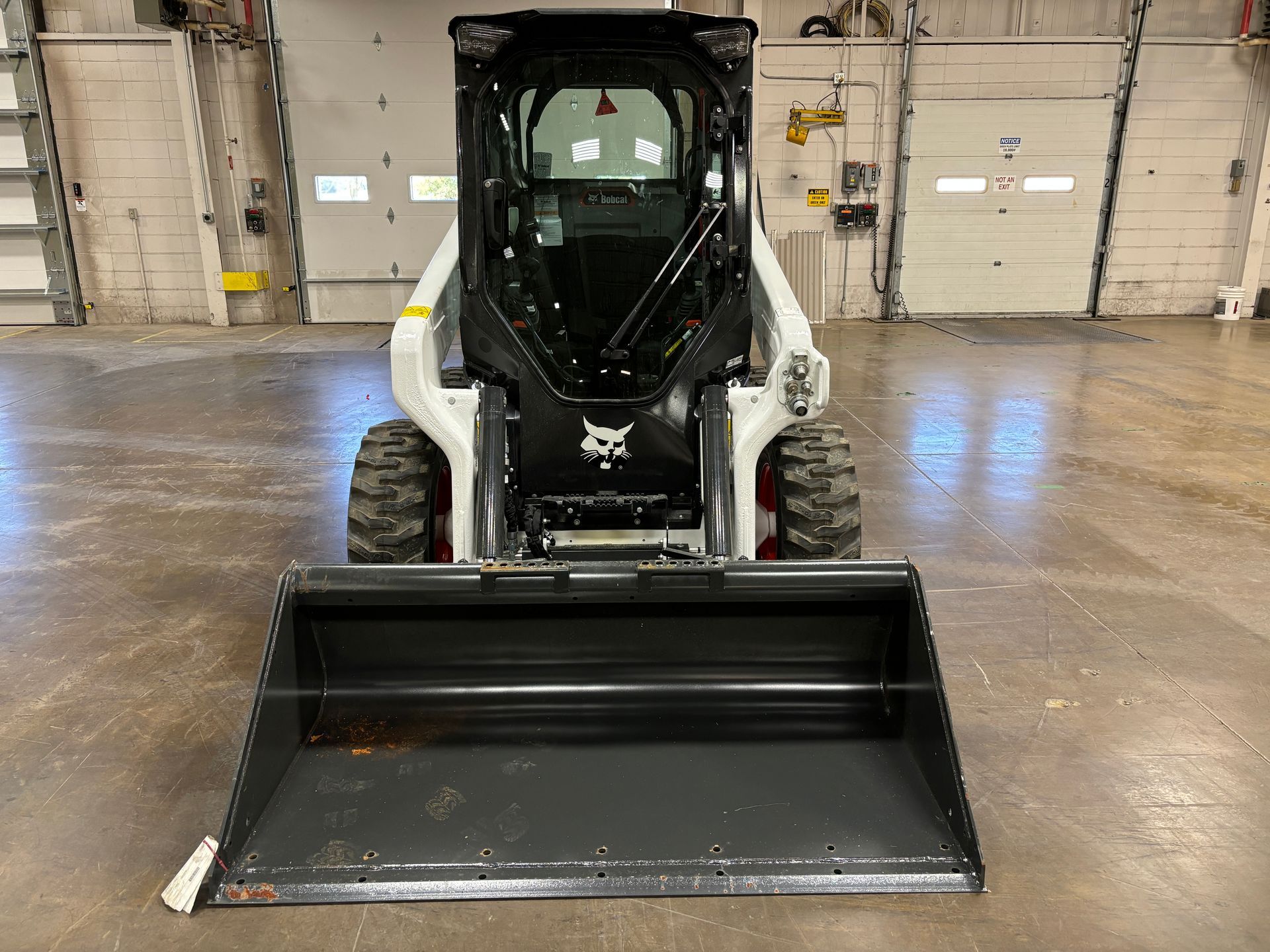 Bobcat skid-steer loader with a black bucket, inside a building with a concrete floor.