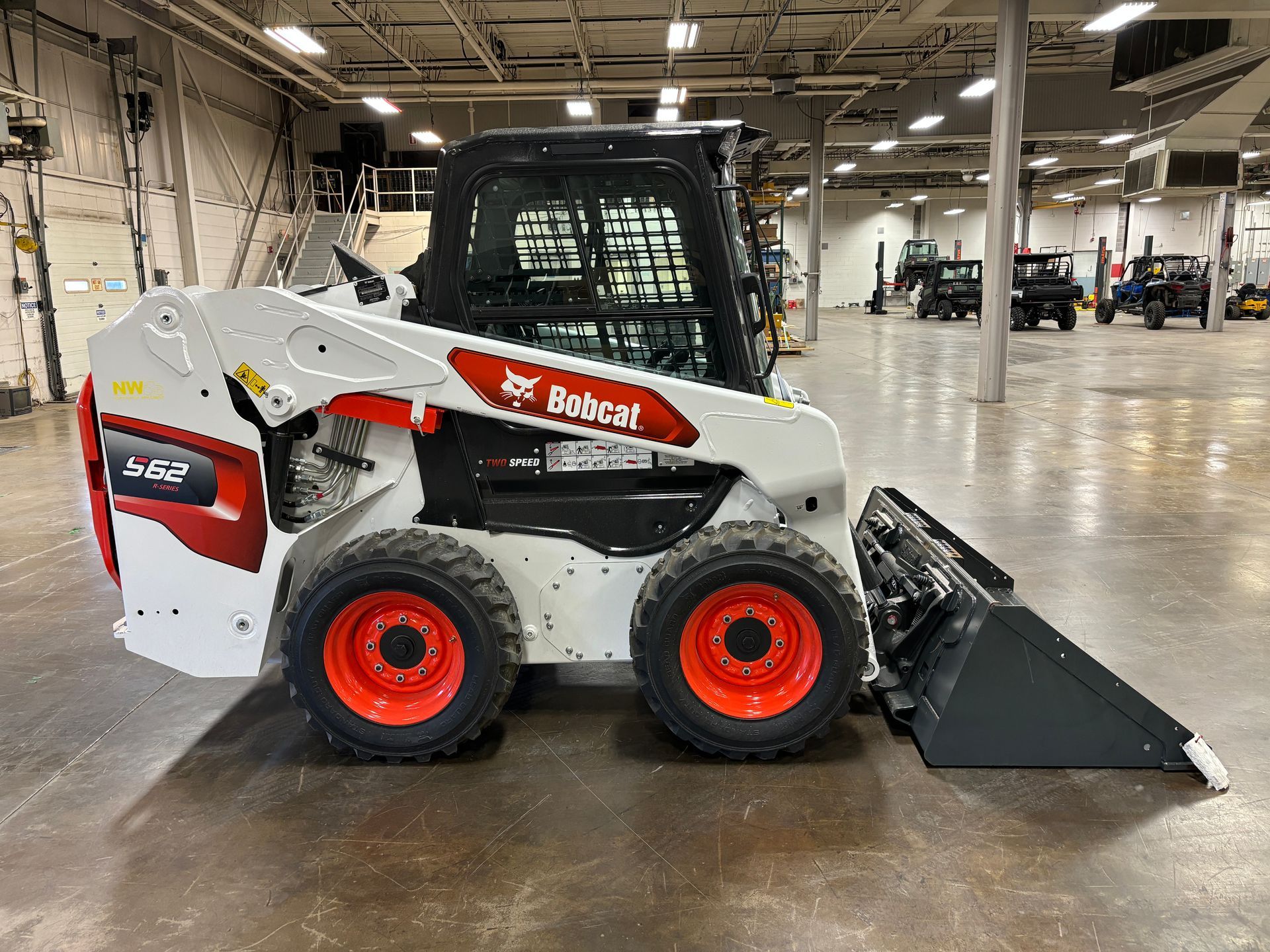 White and red Bobcat skid-steer loader with a bucket, parked indoors.