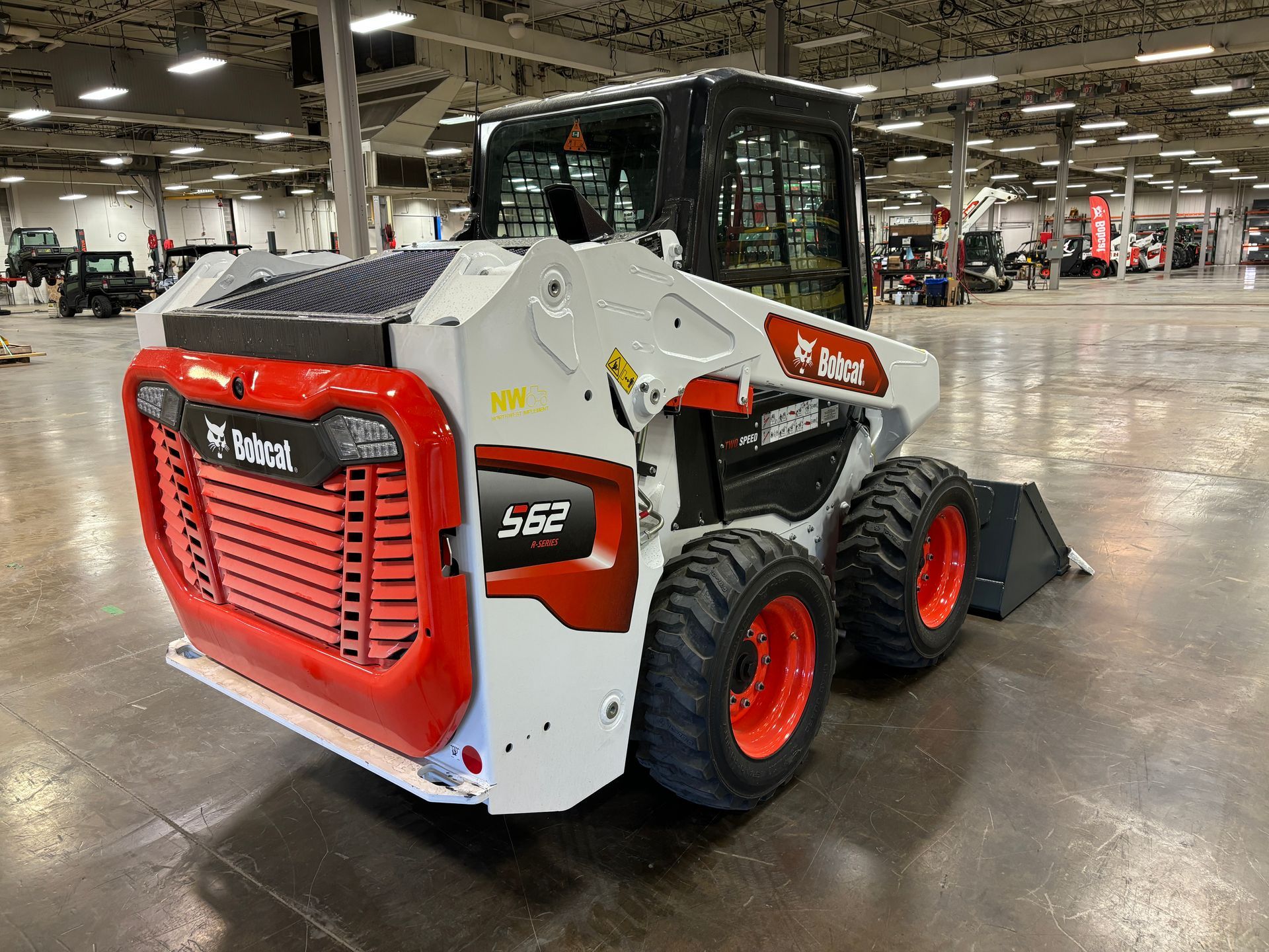 Bobcat S562 skid-steer loader, white and orange, on display in a large warehouse.