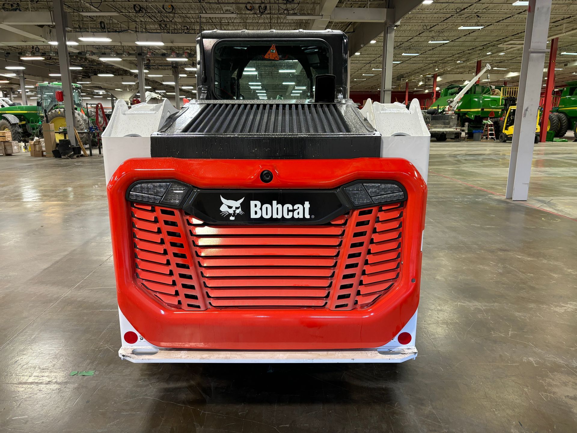 Red and white Bobcat skid-steer loader in a warehouse setting, front view.