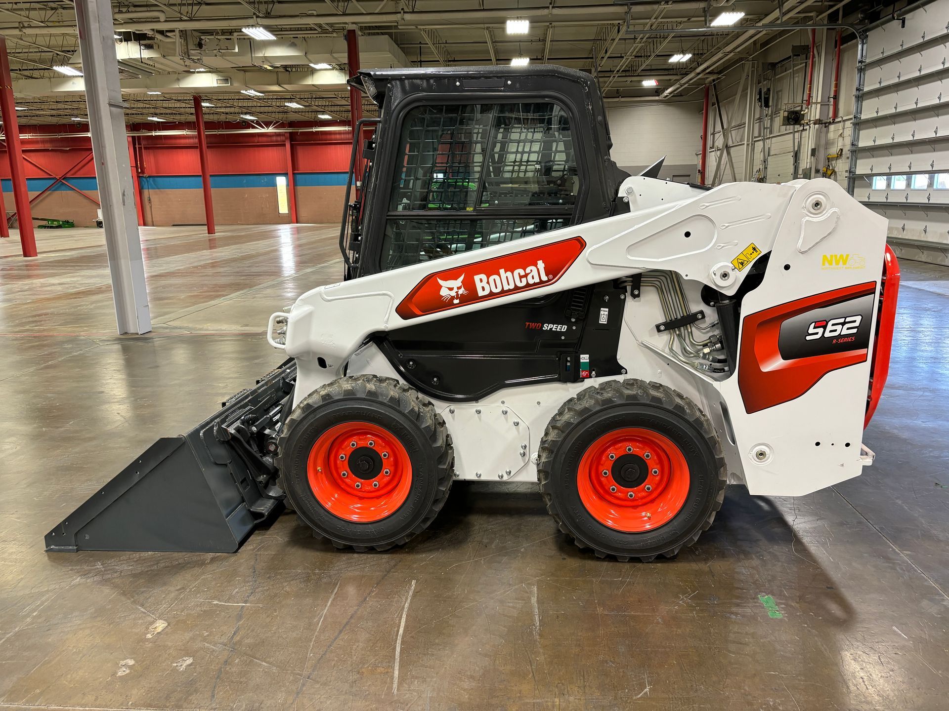 Bobcat S62 skid-steer loader, white and red, on a concrete floor in a large, open industrial space.