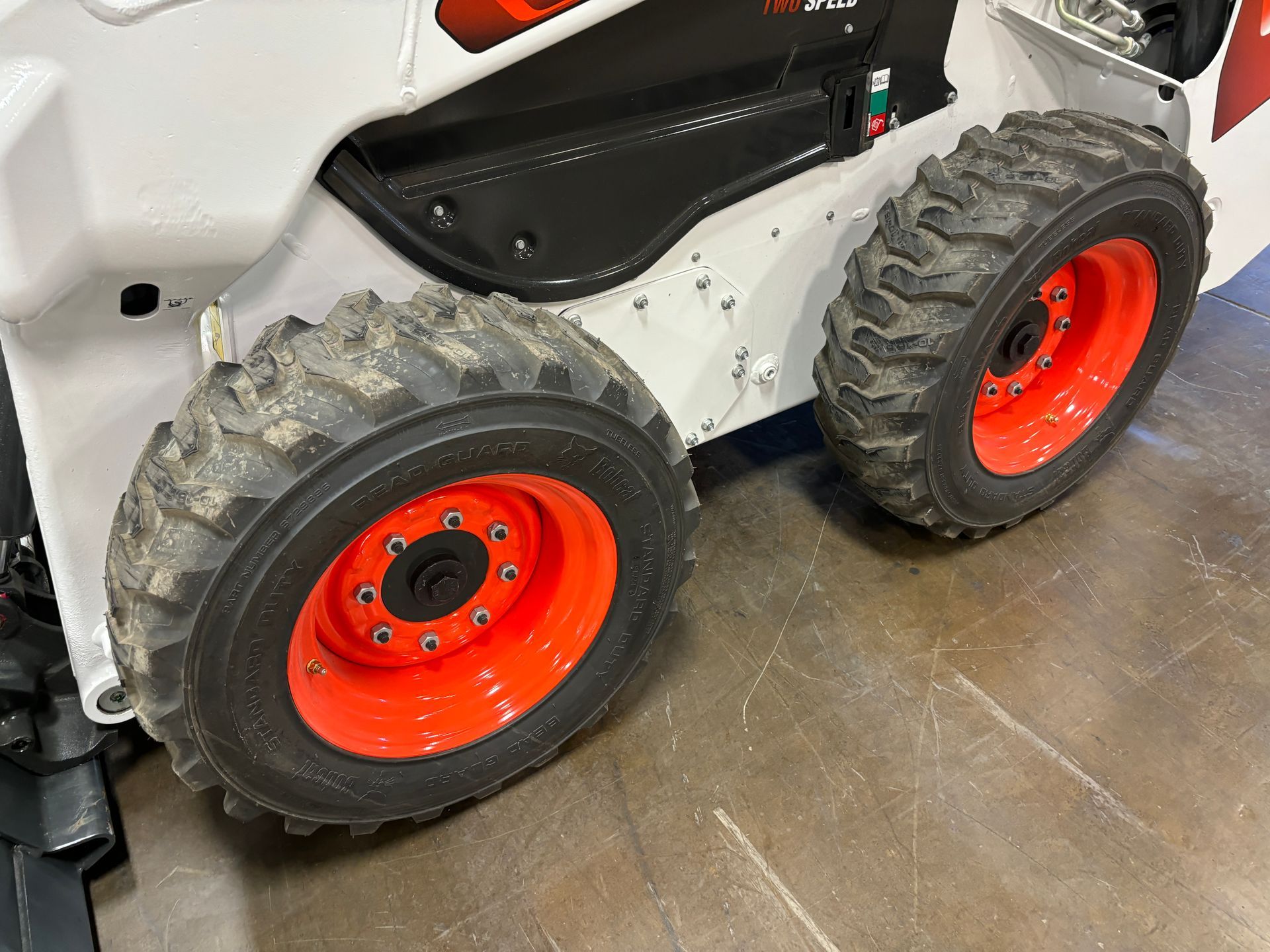 Bobcat skid-steer loader's wheels. Tires on orange rims, against a metal surface.