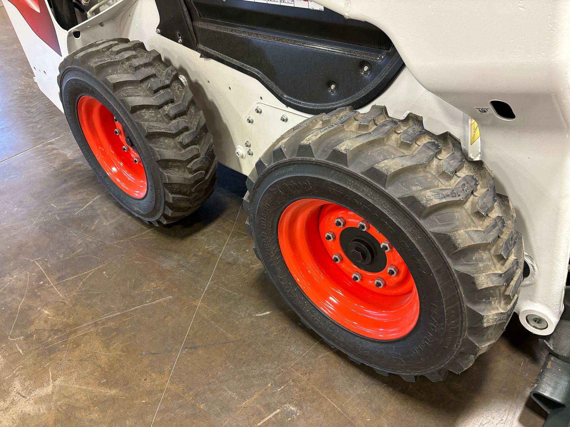 Bobcat skid-steer loader's orange wheels and black tires. Gray and white body, inside a garage or workshop.