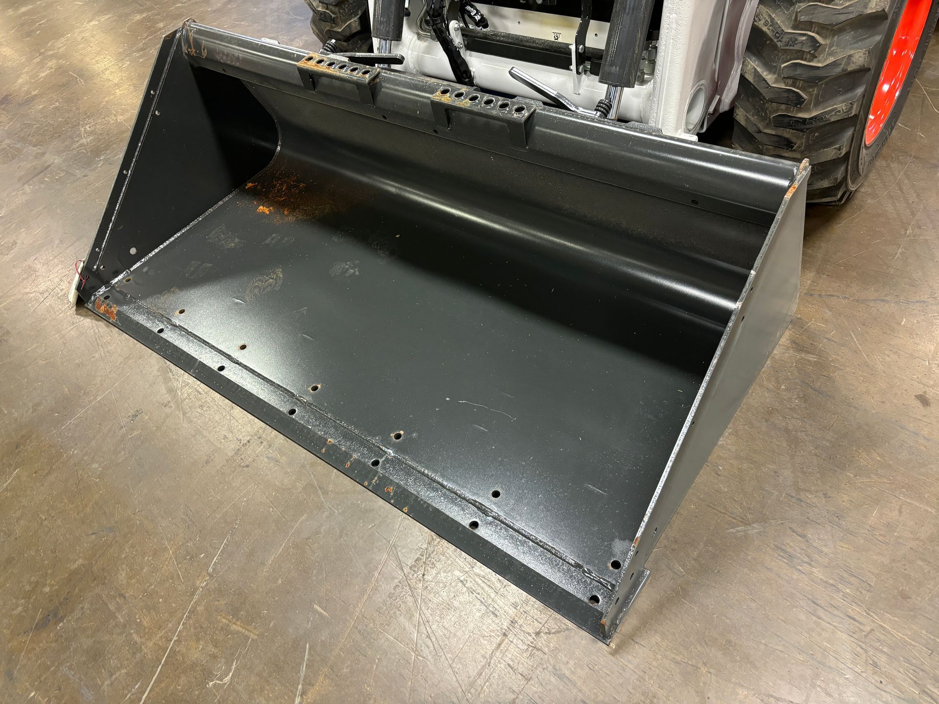 Black skid steer bucket angled on a concrete floor.