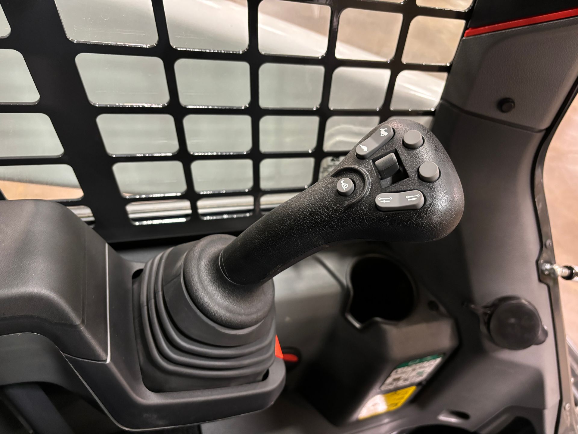 Black joystick control in the cabin of a construction vehicle, with buttons and a rubber boot.