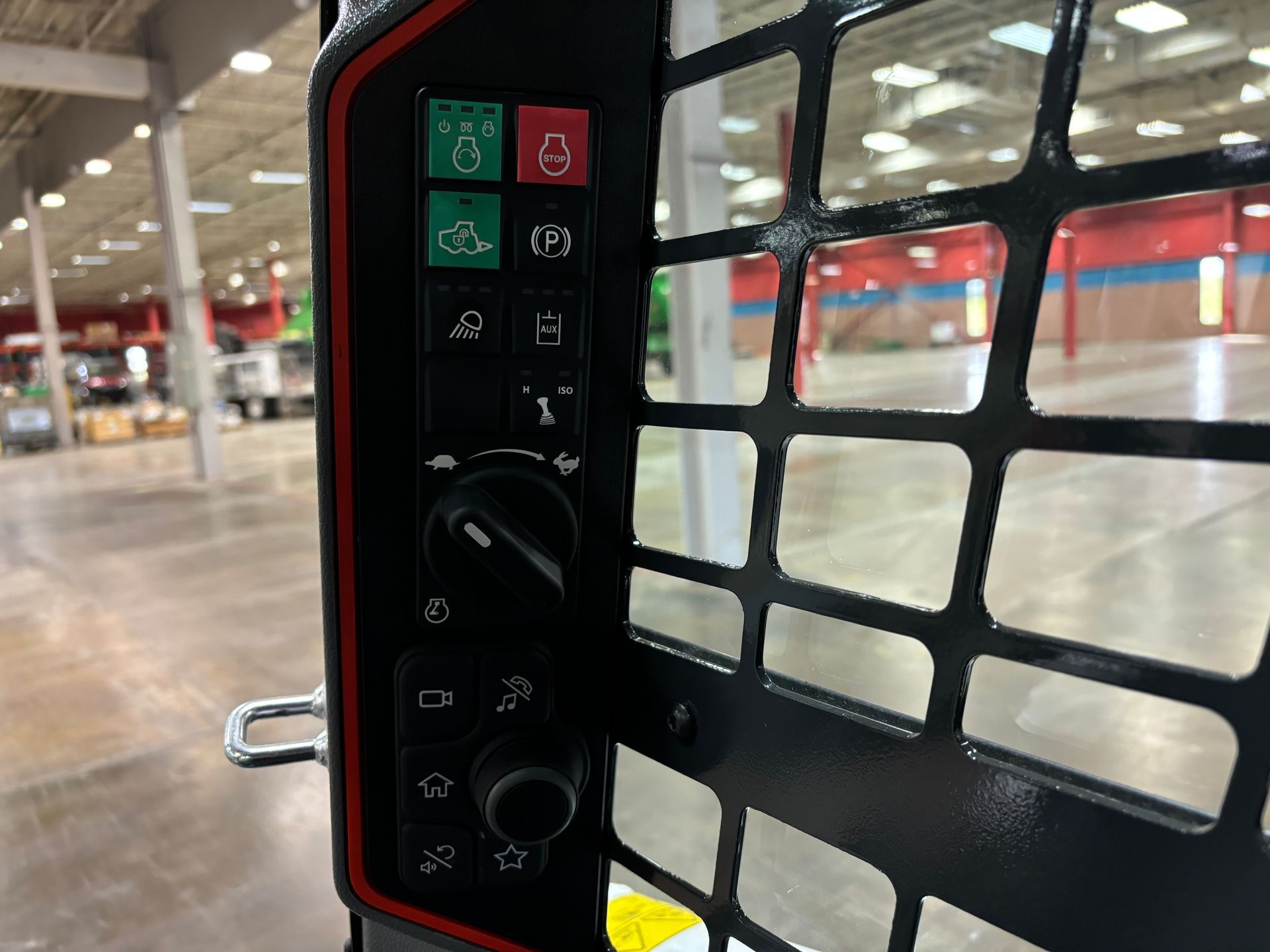 Close-up of a skid steer control panel with buttons and a dial, mounted near a protective grill.