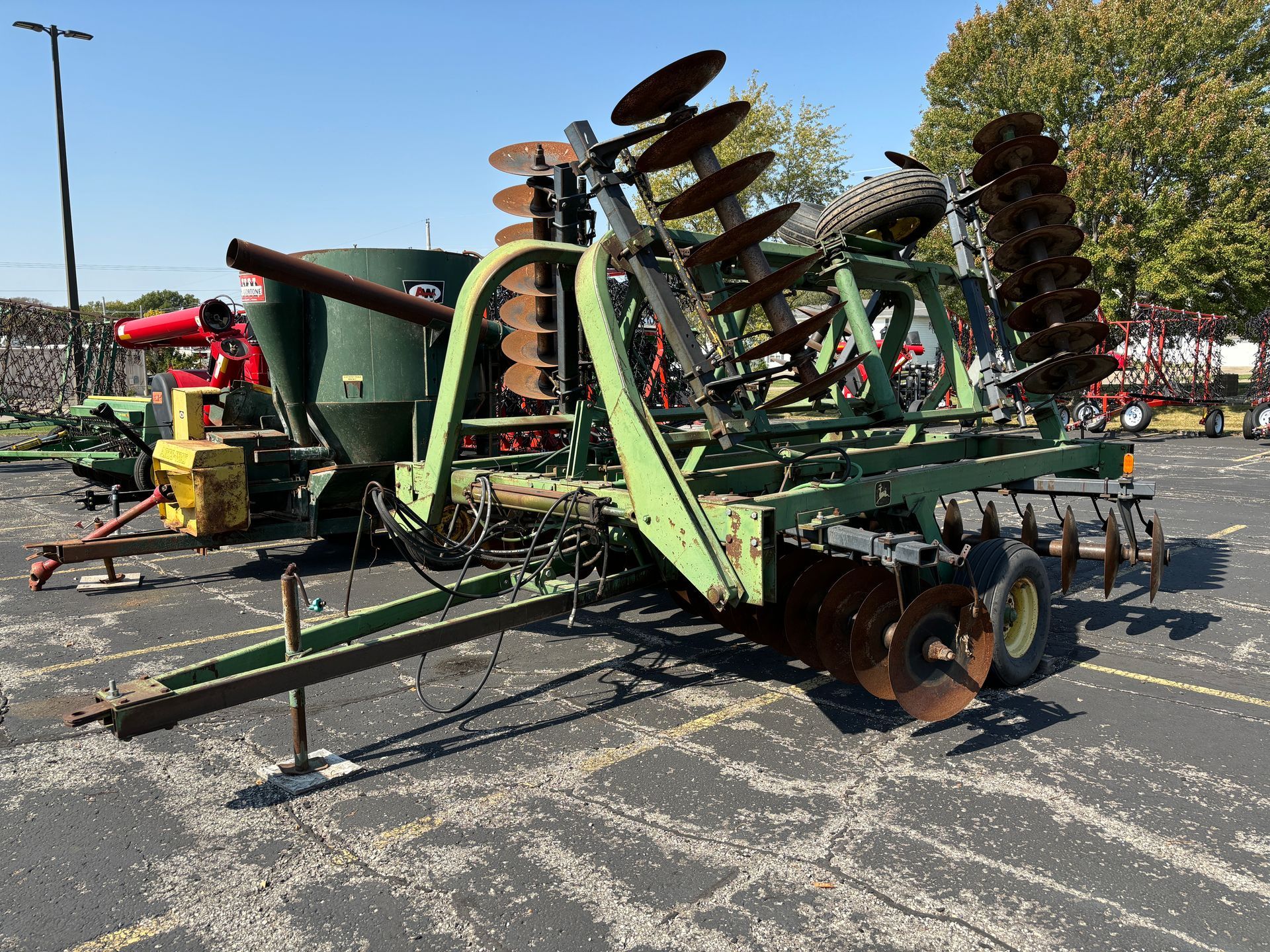 Green and brown farm disc plow in a parking lot on a sunny day.
