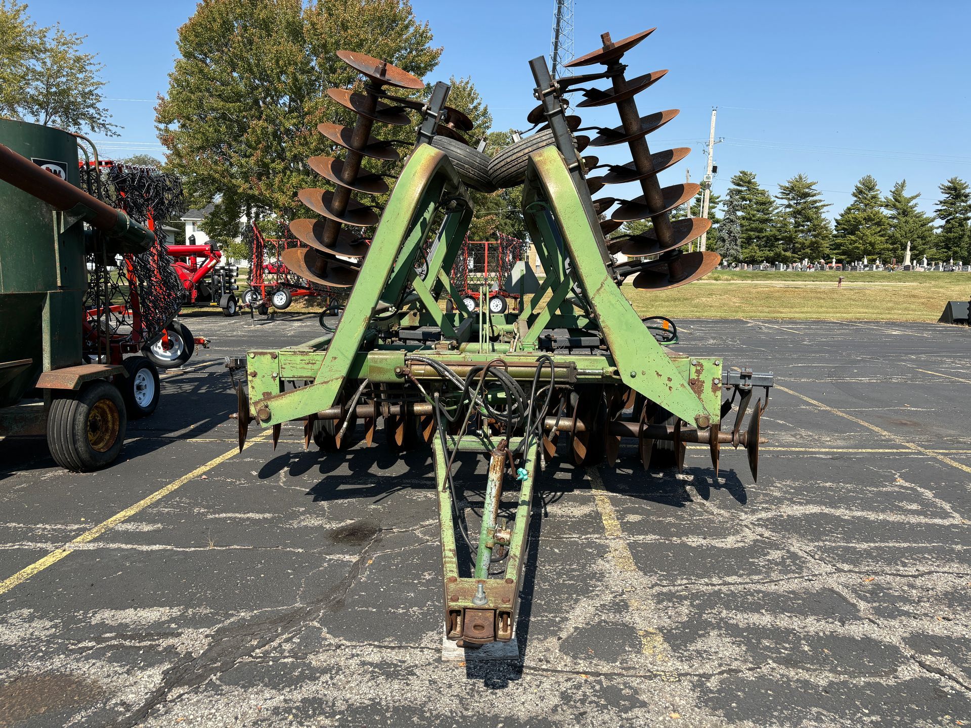 Green farm disc harrow with rusty blades, parked on asphalt.