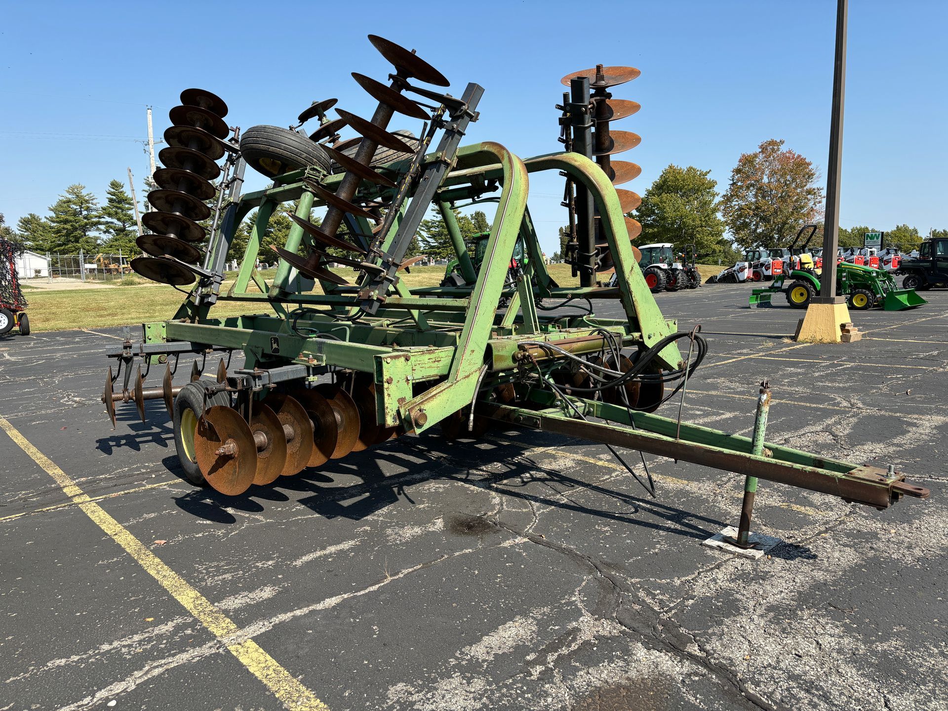 Green John Deere disc harrow on asphalt, outdoors.