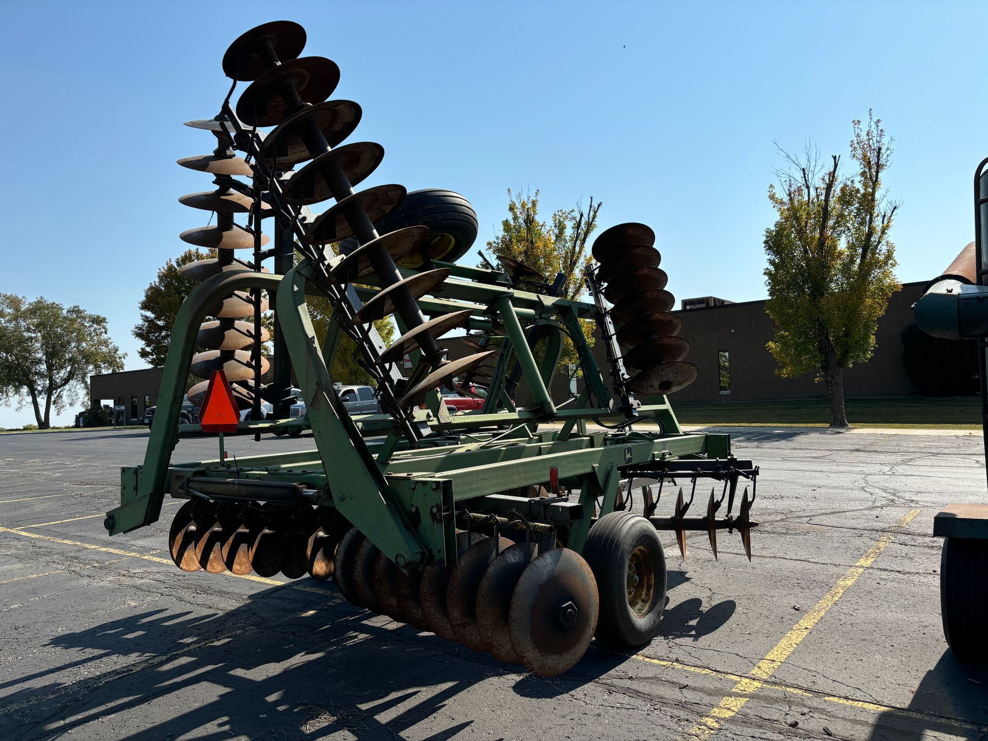 Green agricultural disc harrow on a sunny day in a parking lot.