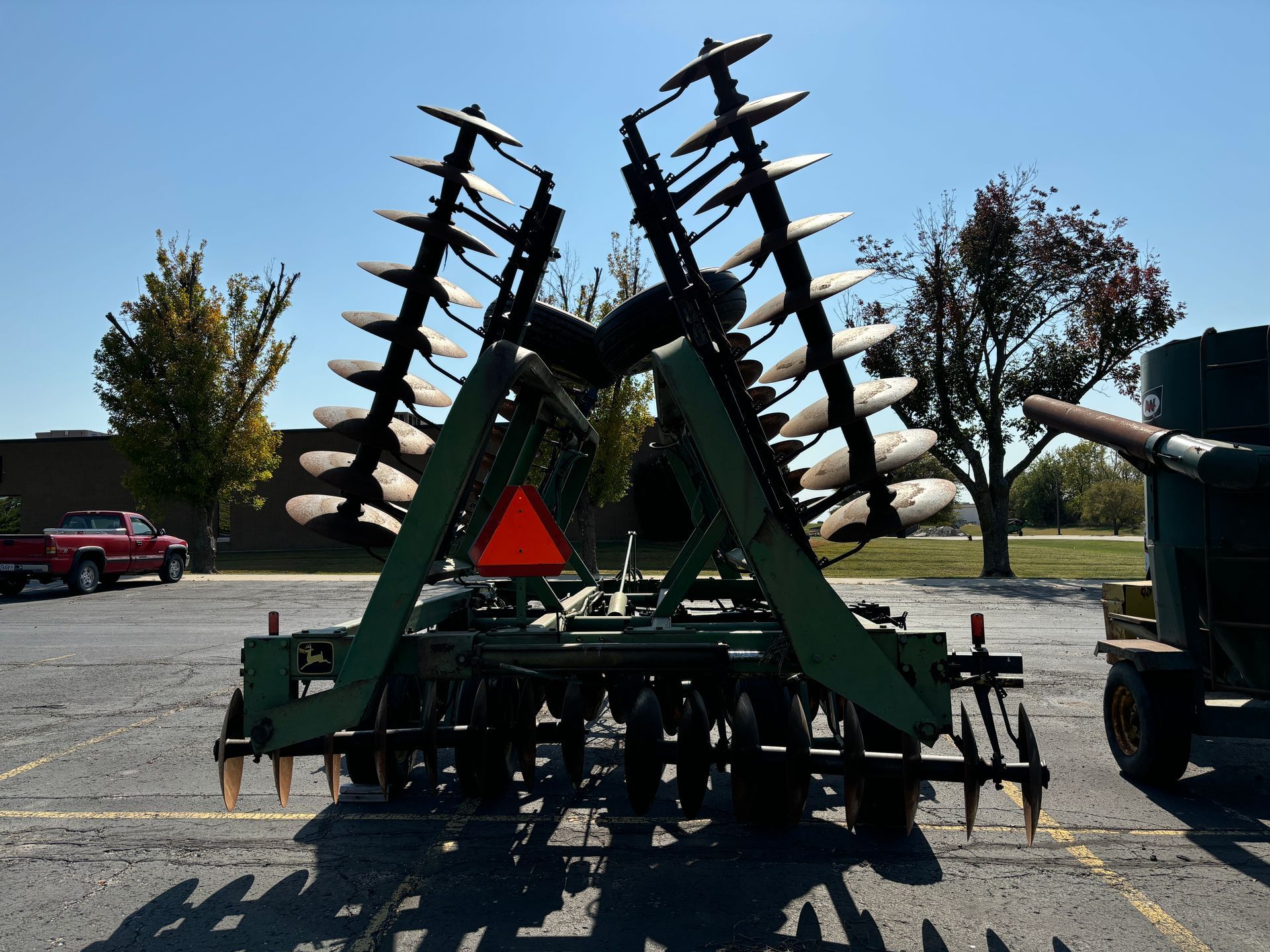 Green disc harrow in a parking lot on a sunny day.