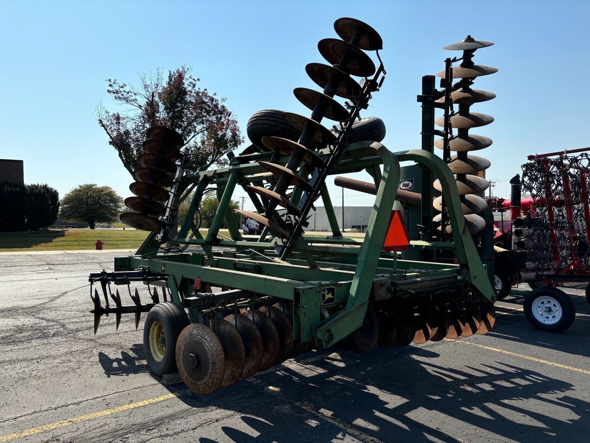 Green farm disk harrow with multiple tilted blades on a sunny day.