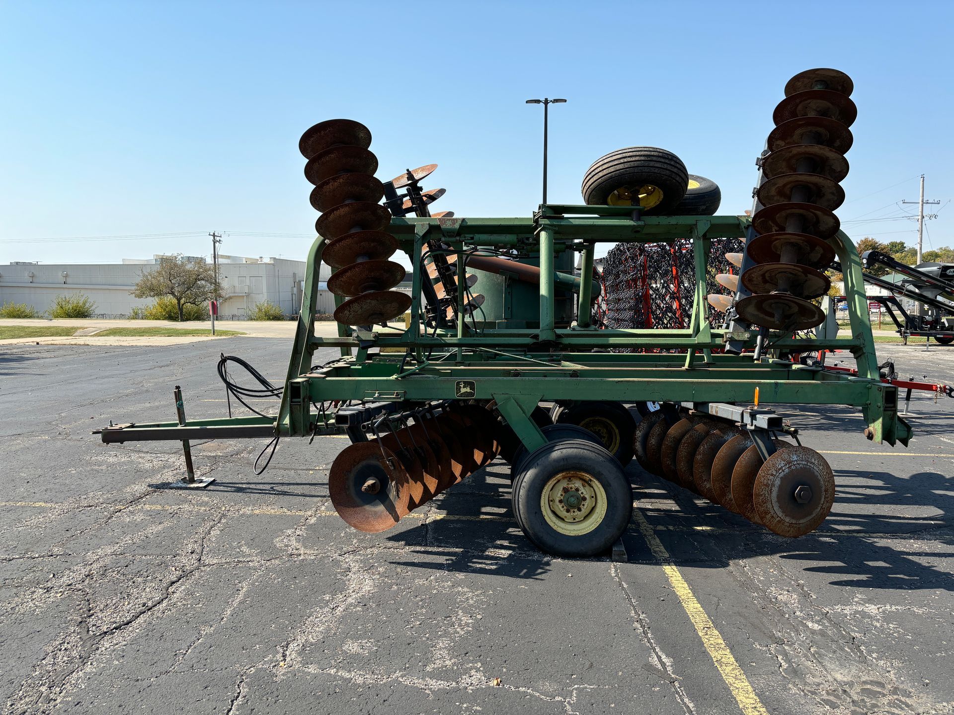 Green farm disc harrow on asphalt, sunny day.