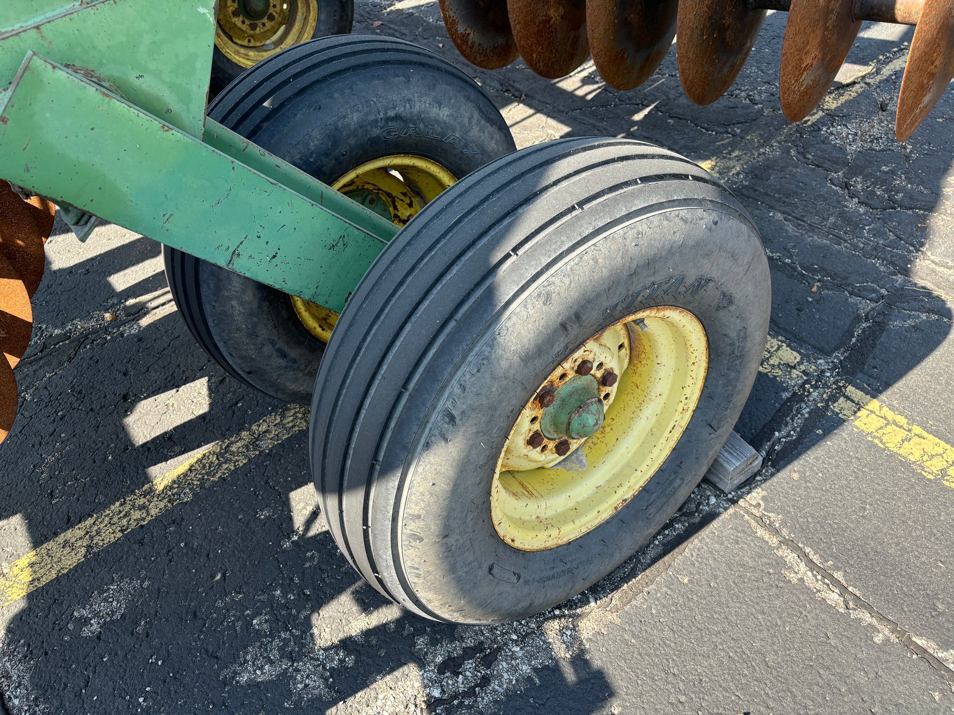 Pair of tractor tires with yellow rims on asphalt. Green metal arm visible.