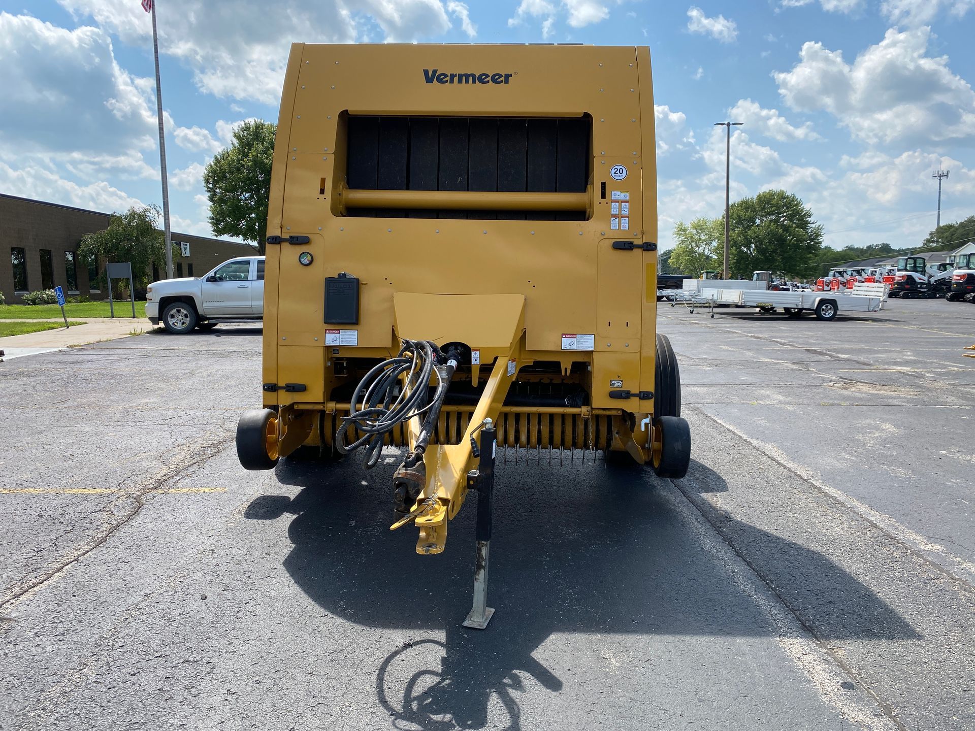 Yellow Vermeer baler parked on asphalt, hitched to a tow arm. Sunny outdoor setting.