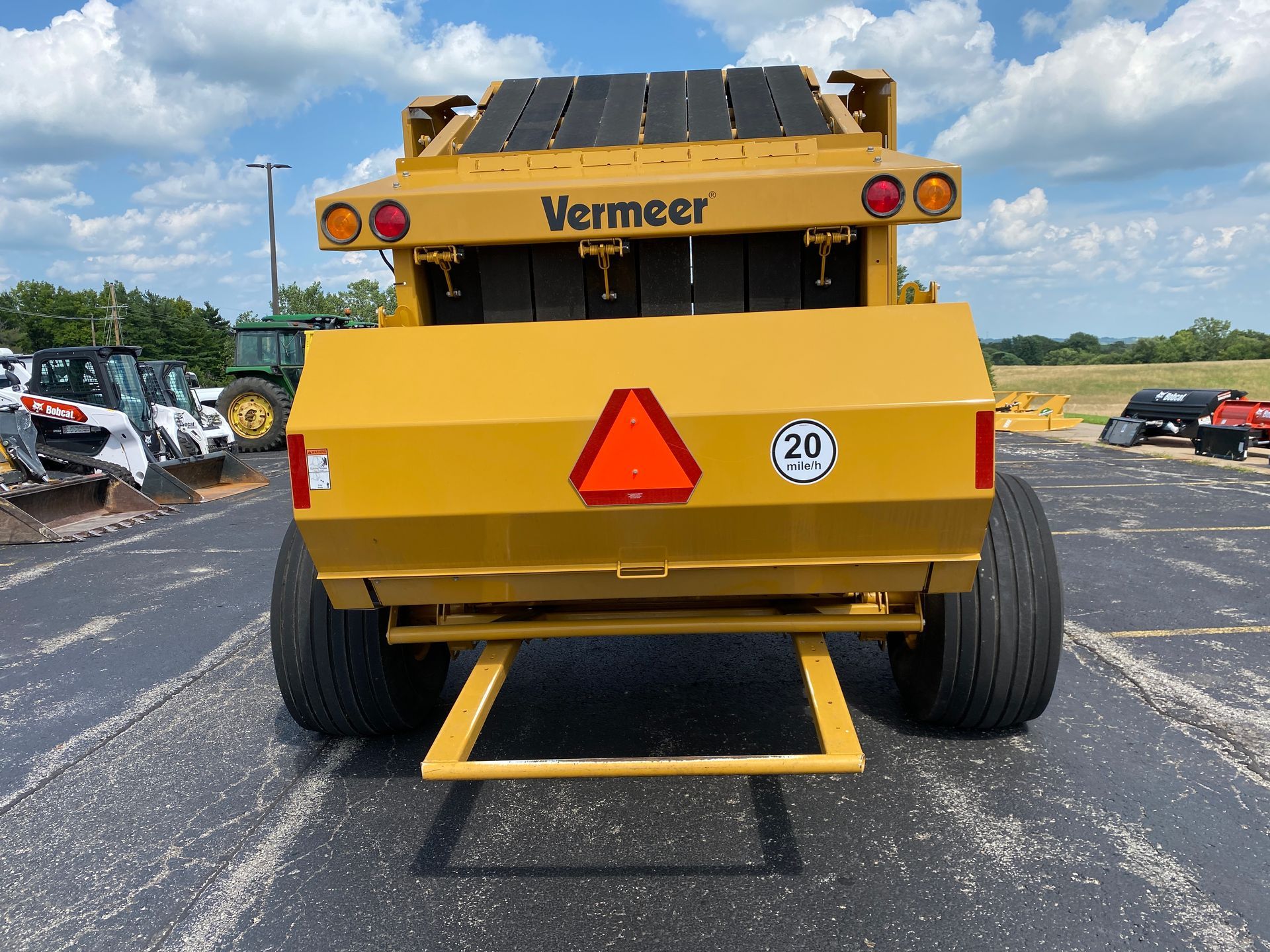 Yellow Vermeer hay baler with large tires, rear view, parked on pavement.