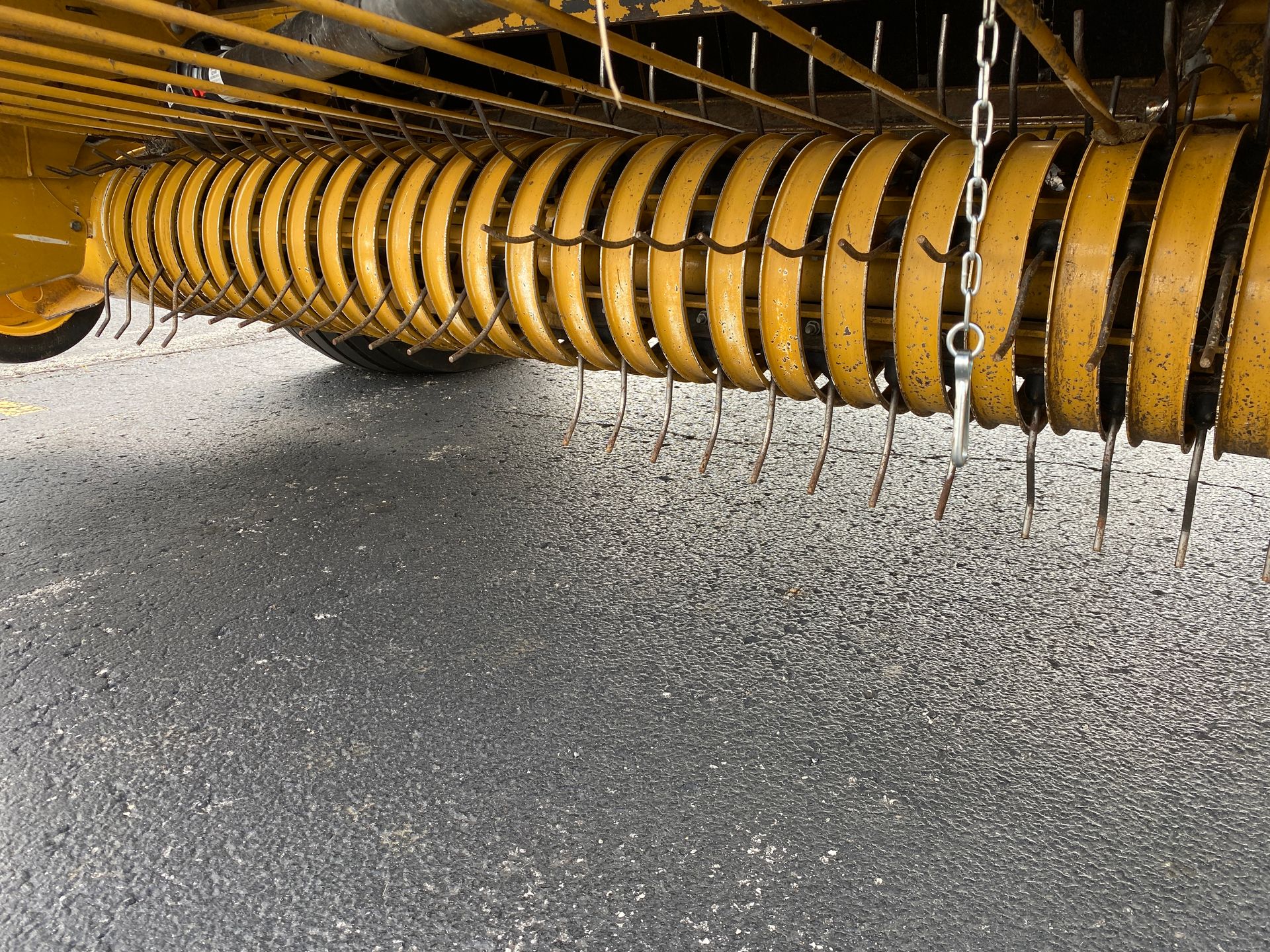 Yellow hay rake tines angled downwards, over asphalt.