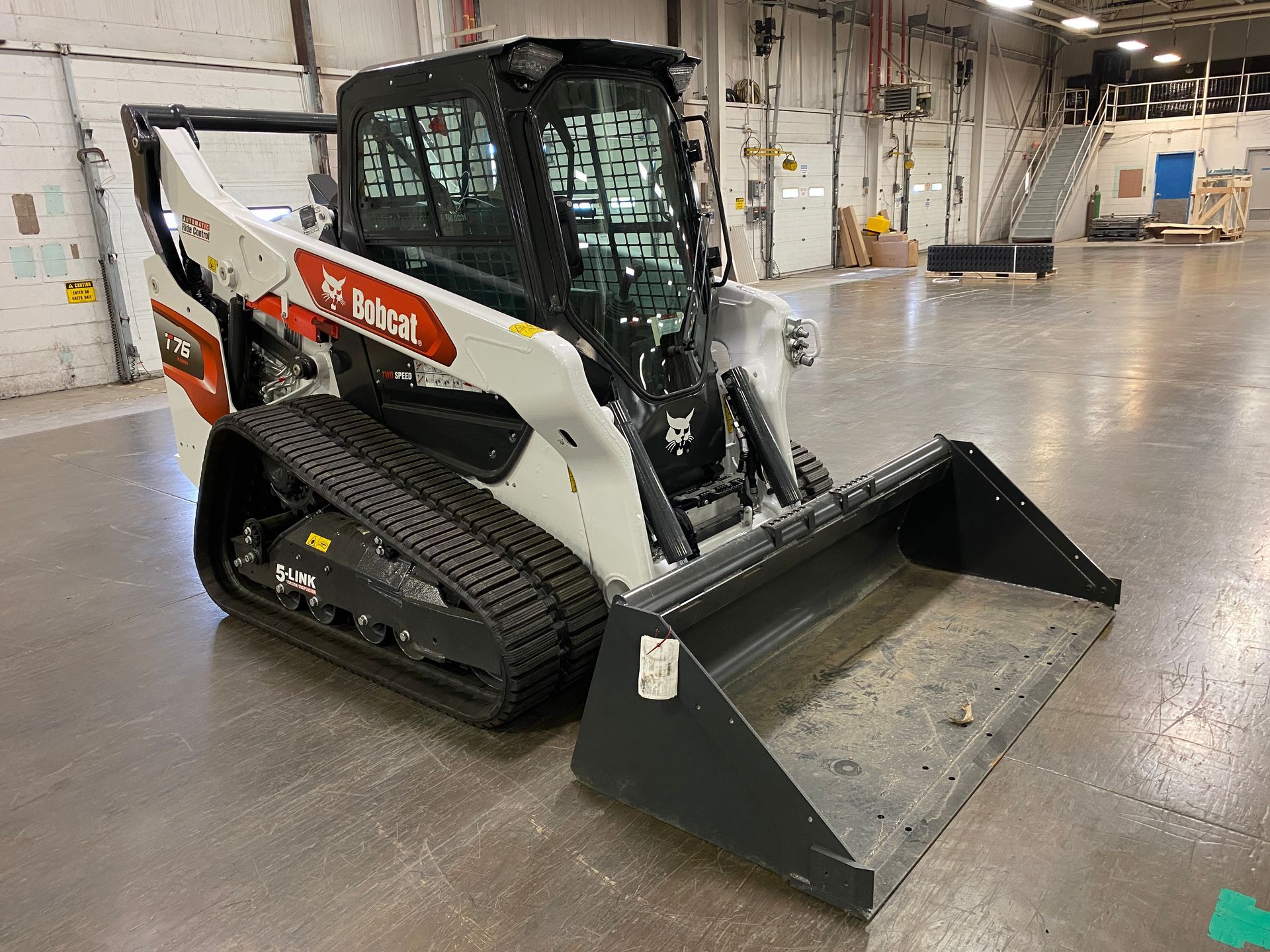 White Bobcat compact track loader with bucket in a warehouse.