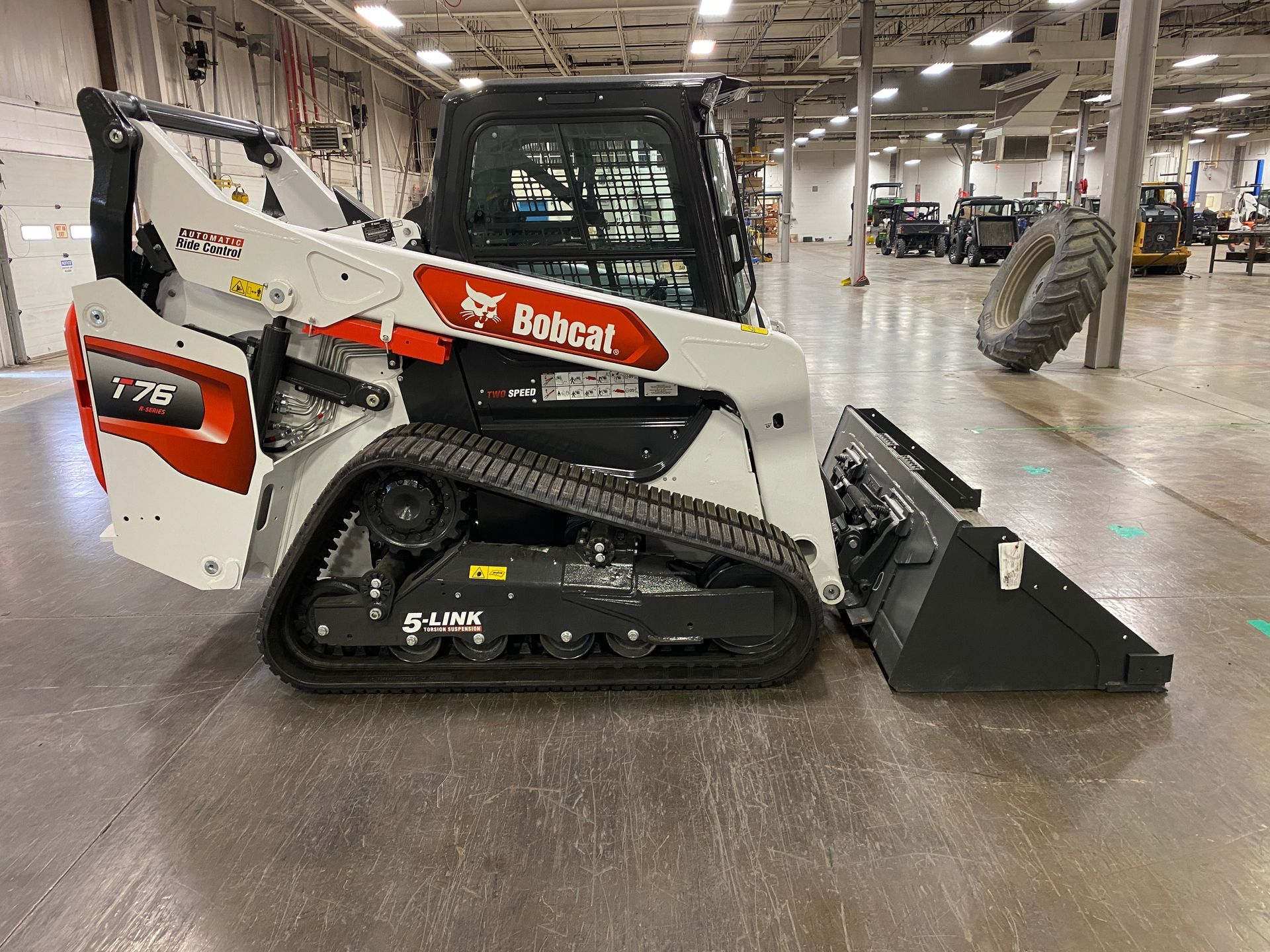 A Bobcat T76 compact track loader with a bucket attachment, indoors, on a gray floor.