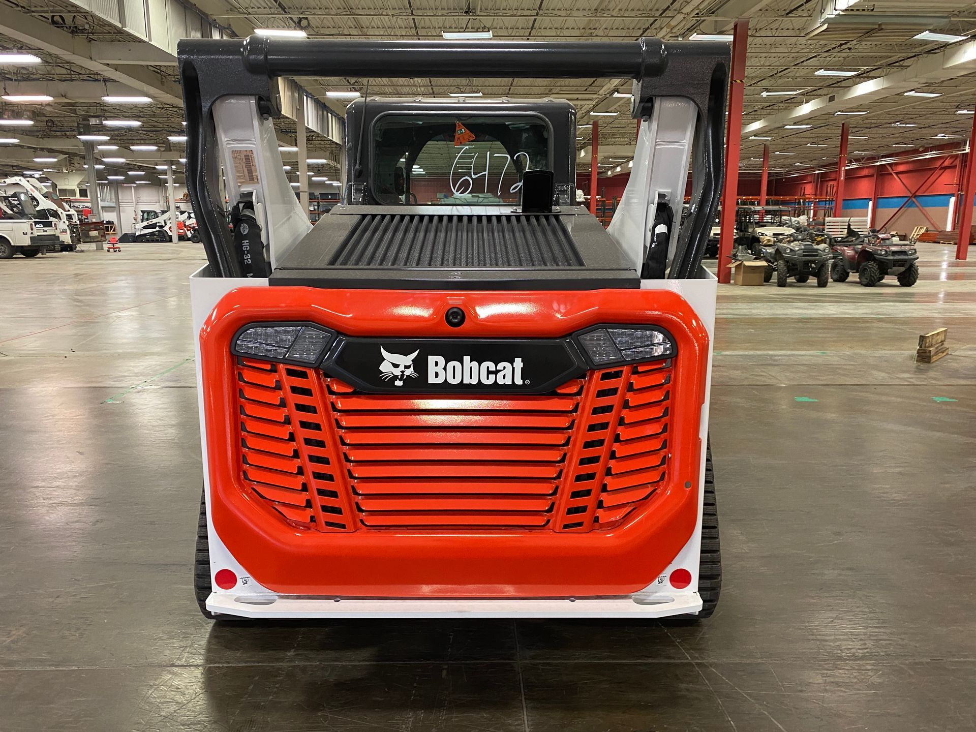 Rear view of a Bobcat skid-steer loader, orange and white with a black grill, parked indoors.