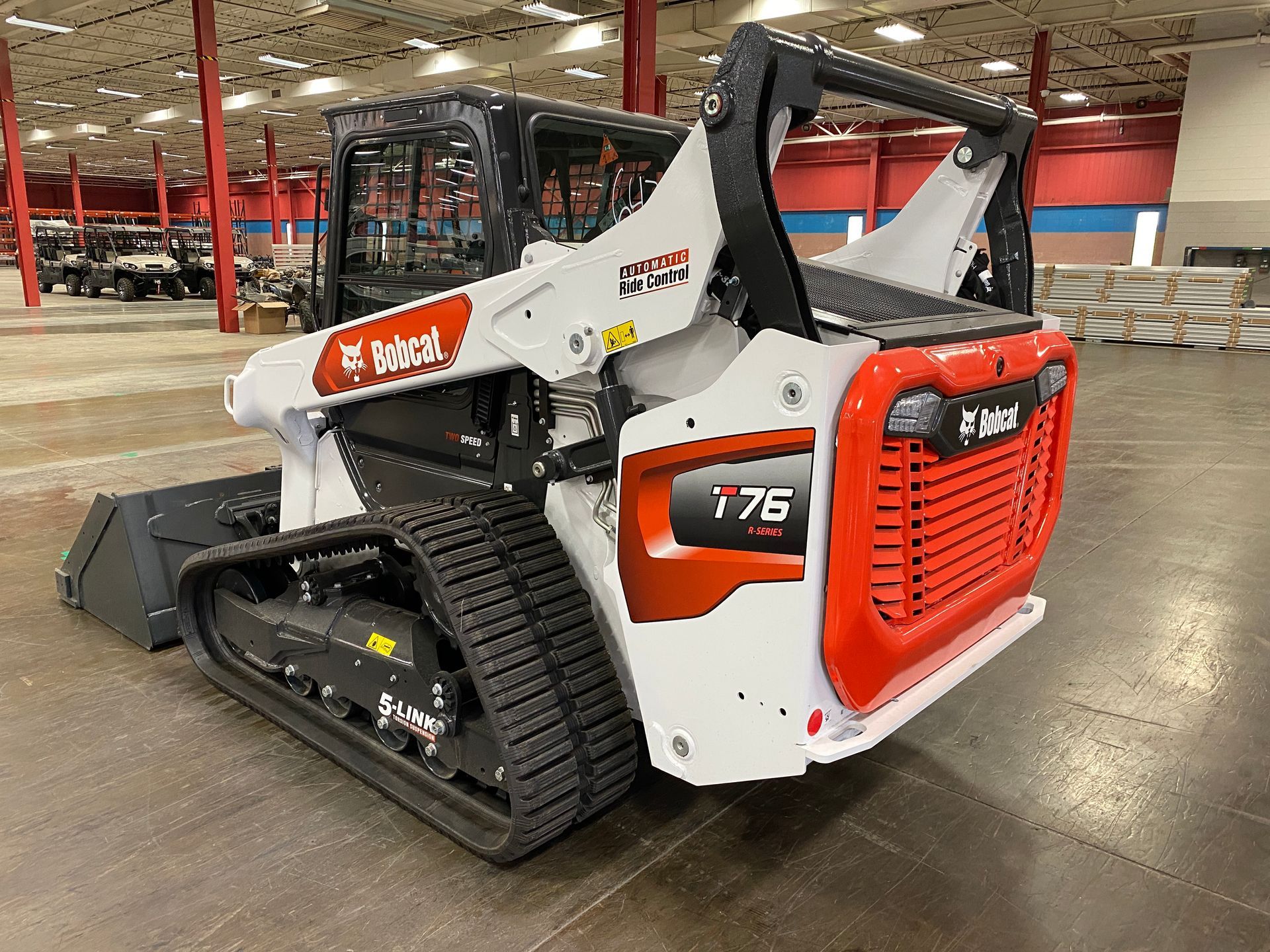 White Bobcat T76 compact track loader with orange accents in a warehouse.