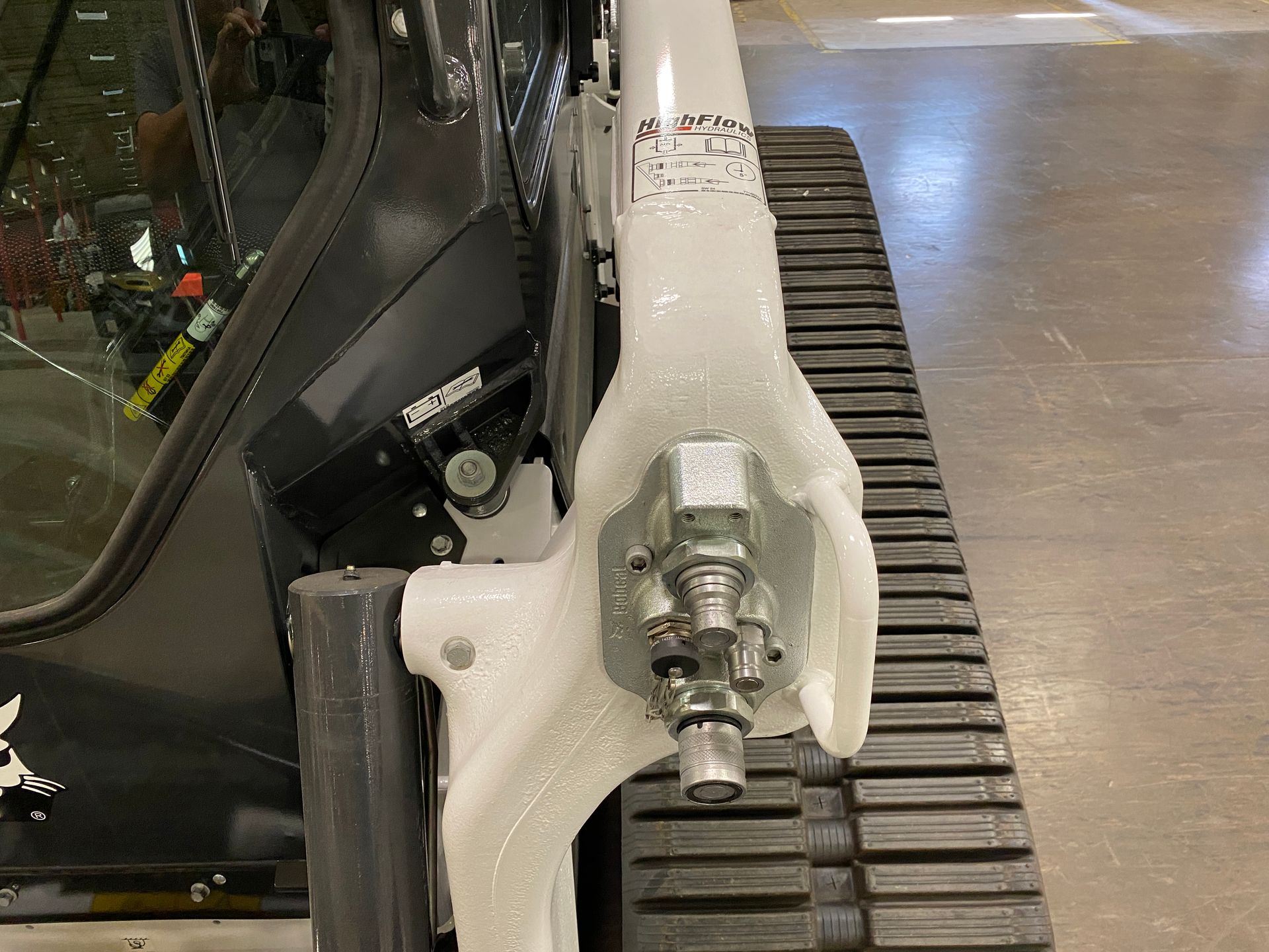 Close-up of a Bobcat skid steer arm and track, showing hydraulic components. Gray, white, and black.