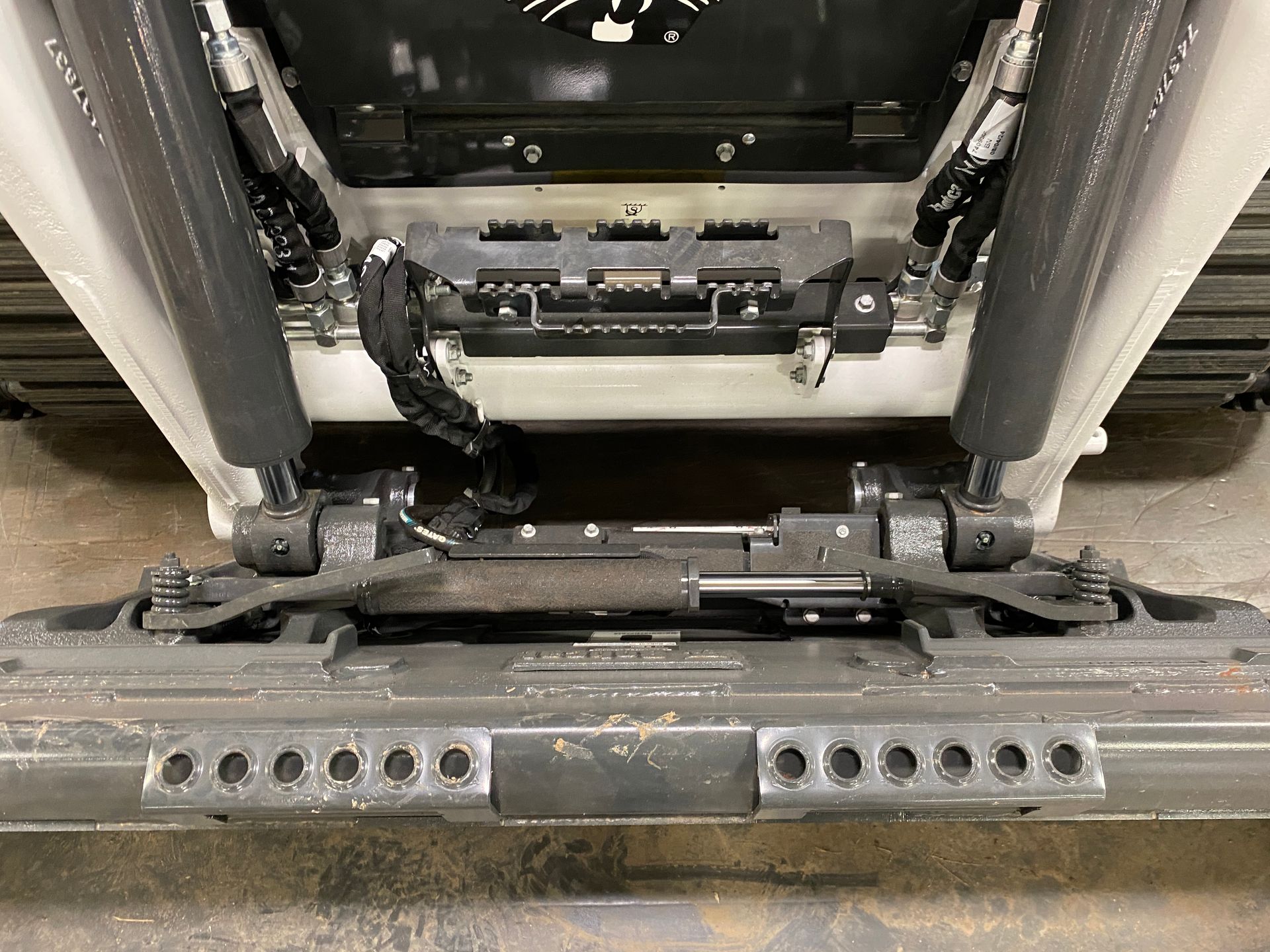 Undercarriage of a snow groomer. Gray metal frame with black suspension components and tracks.