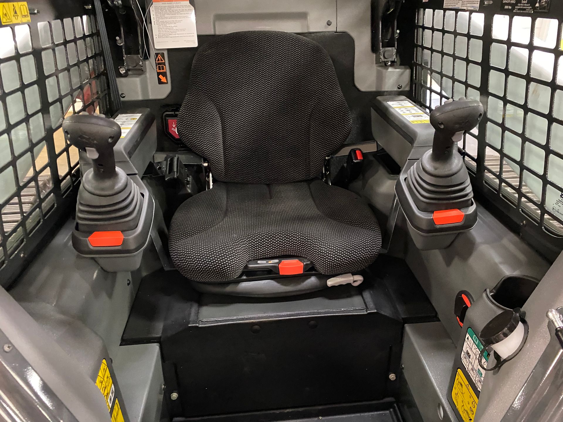 Interior view of a skid steer loader cab with black seat, joysticks, and safety cage.