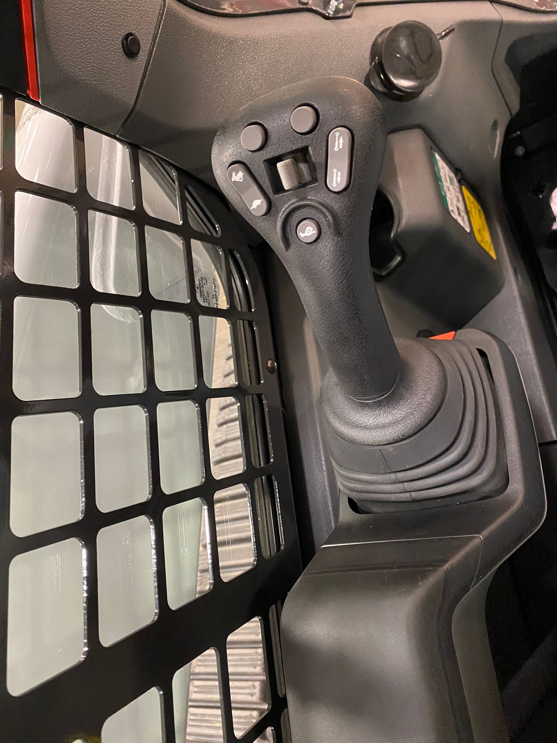 Black joystick controller in the cab of a skid steer loader, with several buttons and a protective cage.