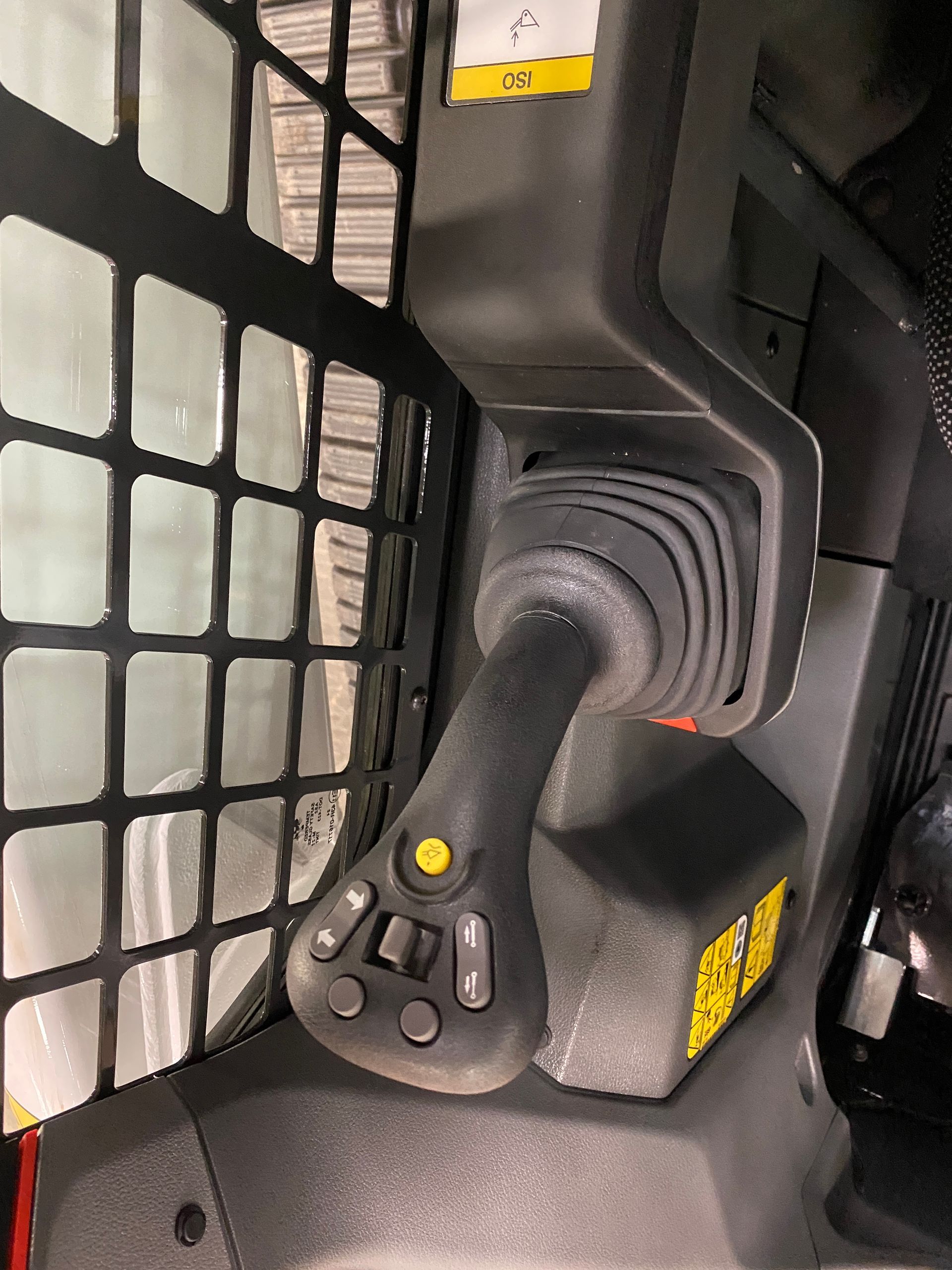Skid steer joystick with buttons and safety cage; black and yellow details.
