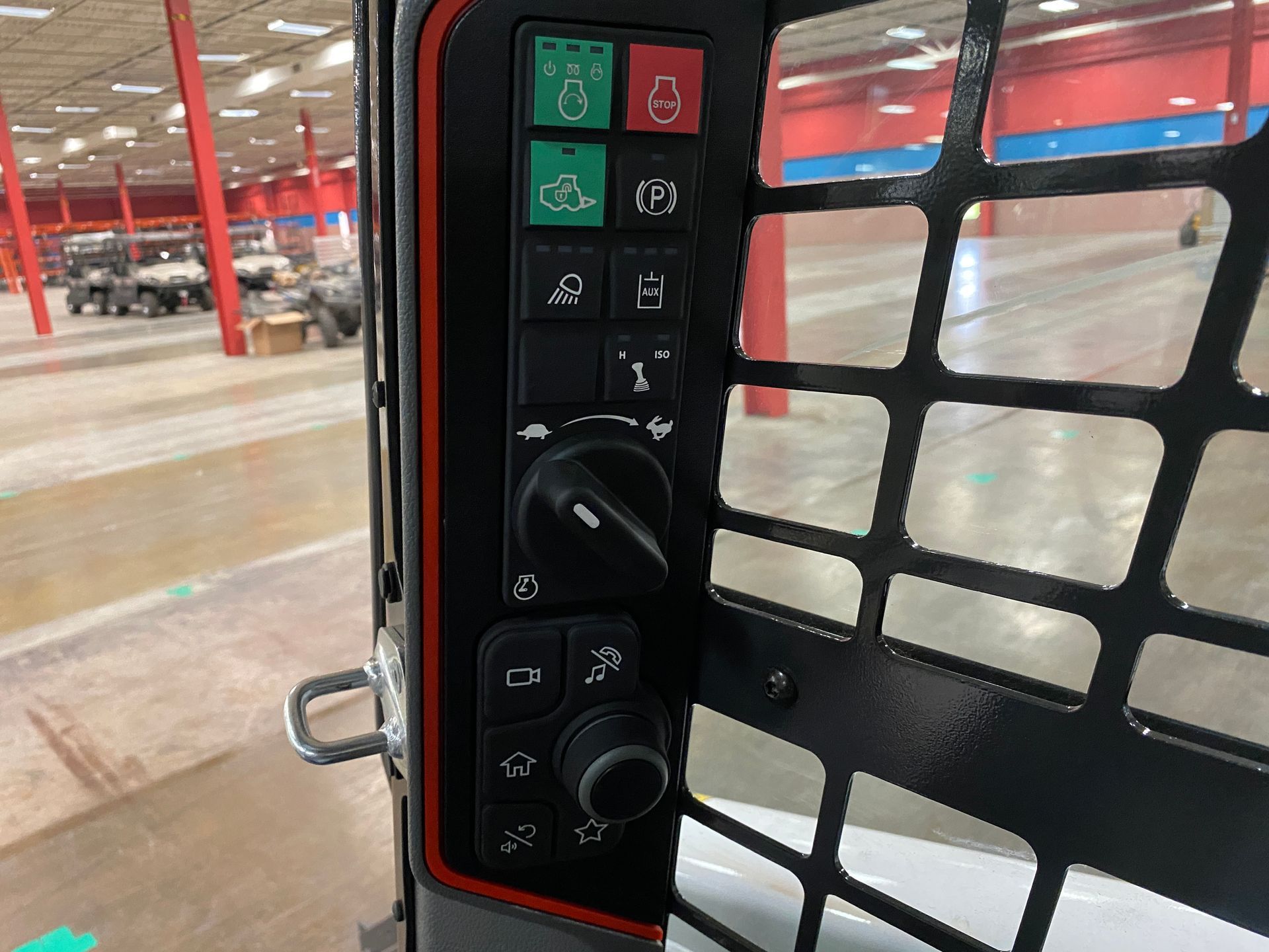 Control panel in a construction vehicle with various buttons, dials, and a safety cage.