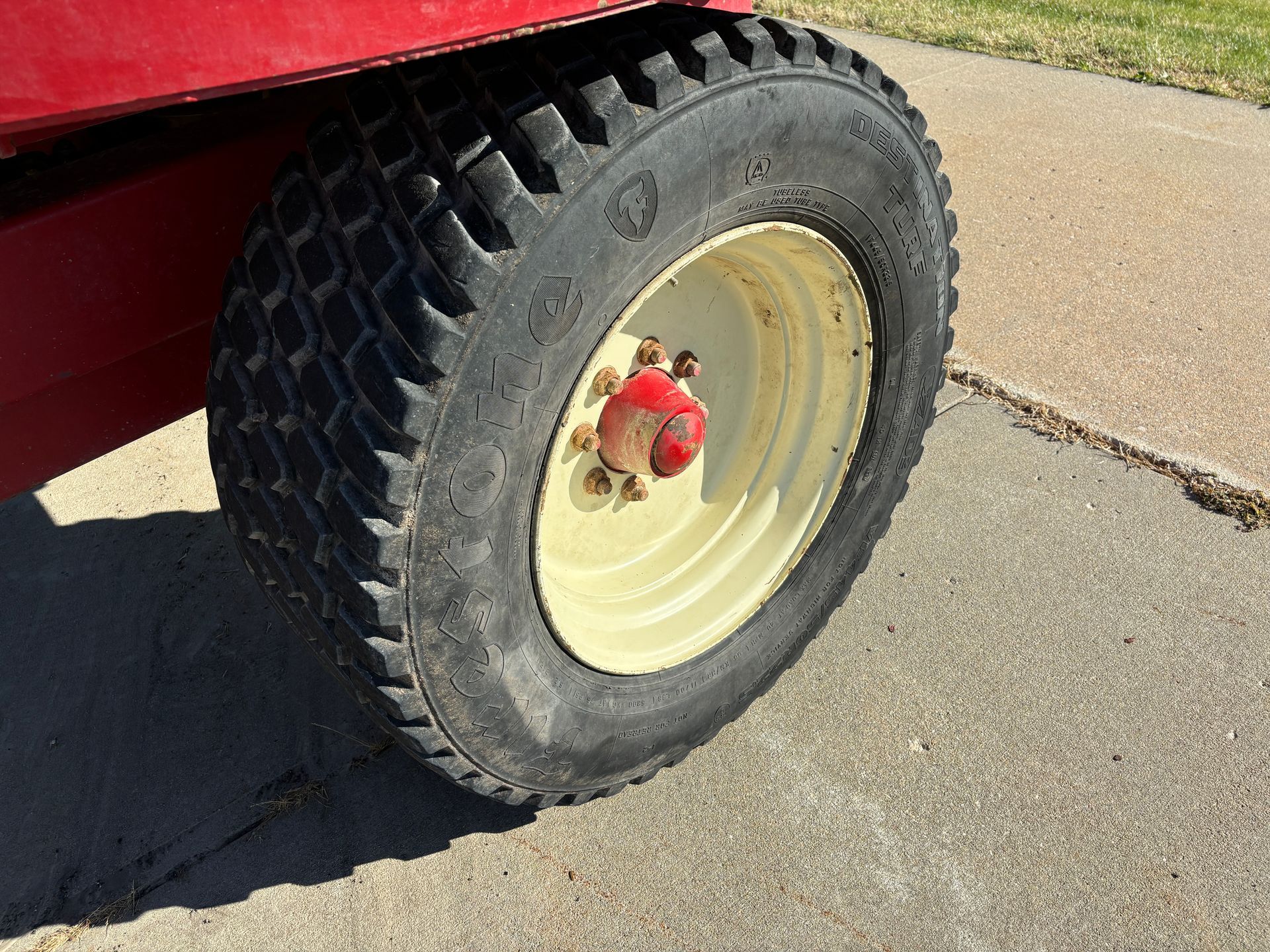 Close-up of a red mixer wagon wheel with a black tire, on a concrete surface.