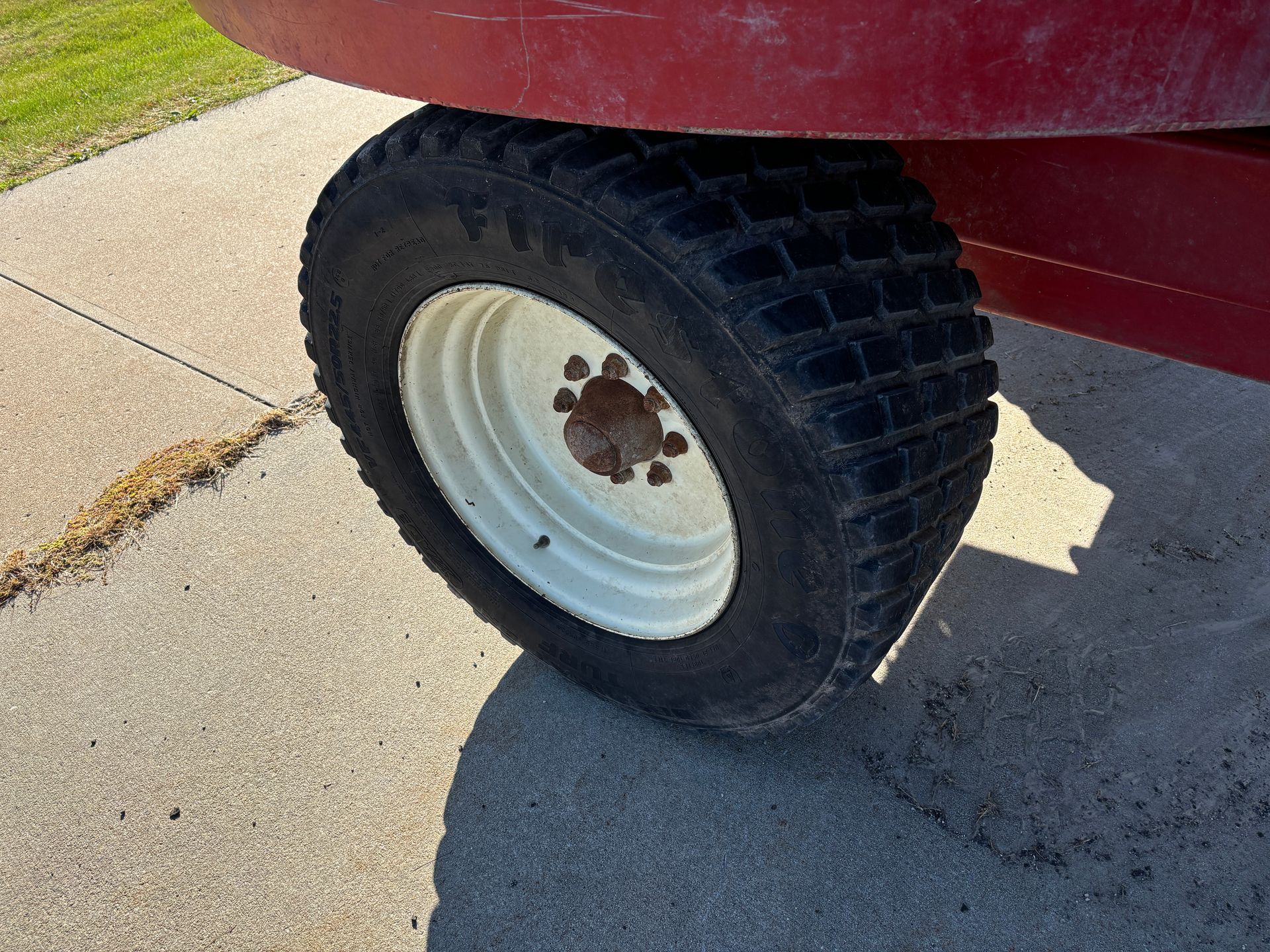 Close-up of a red mixer wagon wheel with a black tire, on a concrete surface.