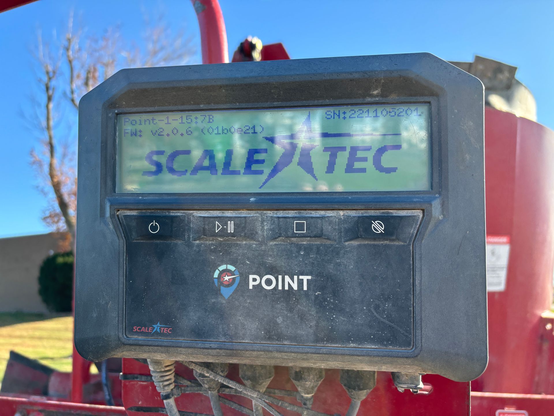 Close-up of a black Scale Tec control panel on red mixer wagon, displaying data and buttons.
