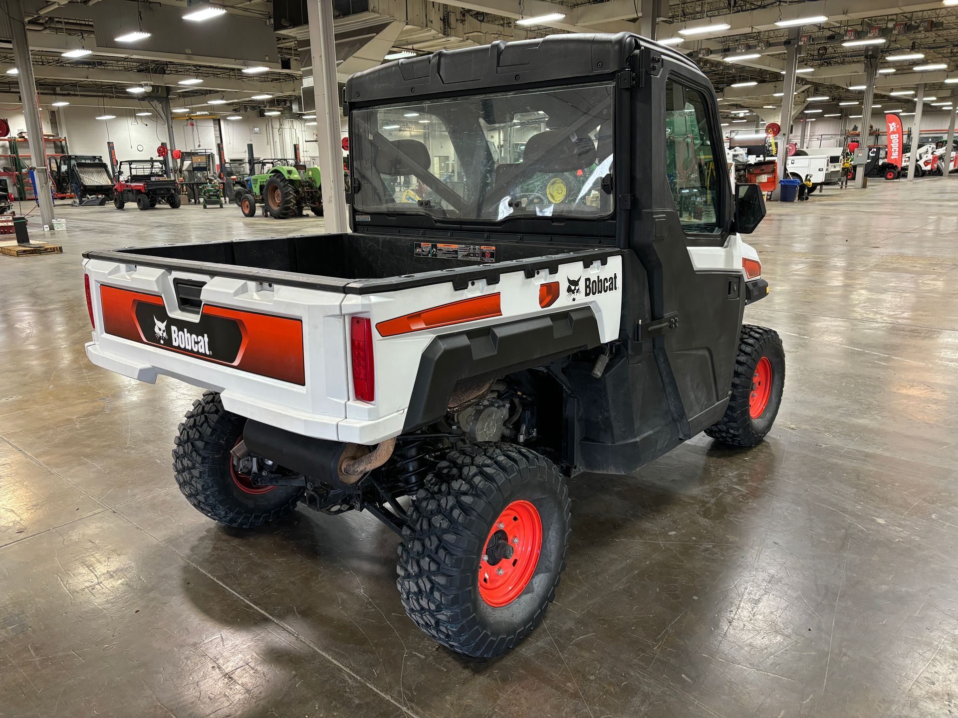 White and black Bobcat utility vehicle with orange accents and tires in a large warehouse.