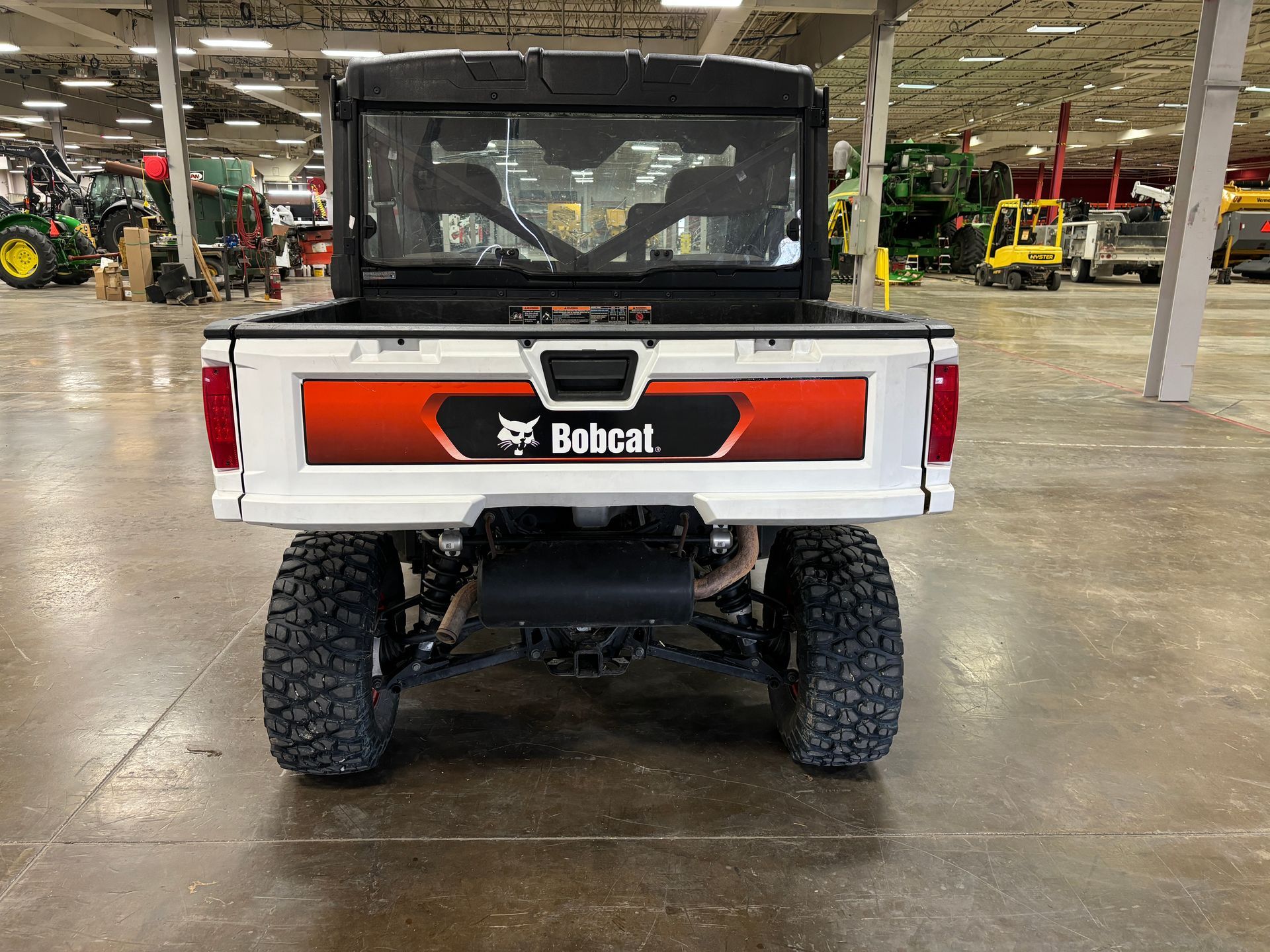White Bobcat utility vehicle from the rear. Black roll cage and bed. Orange and black logo on tailgate.