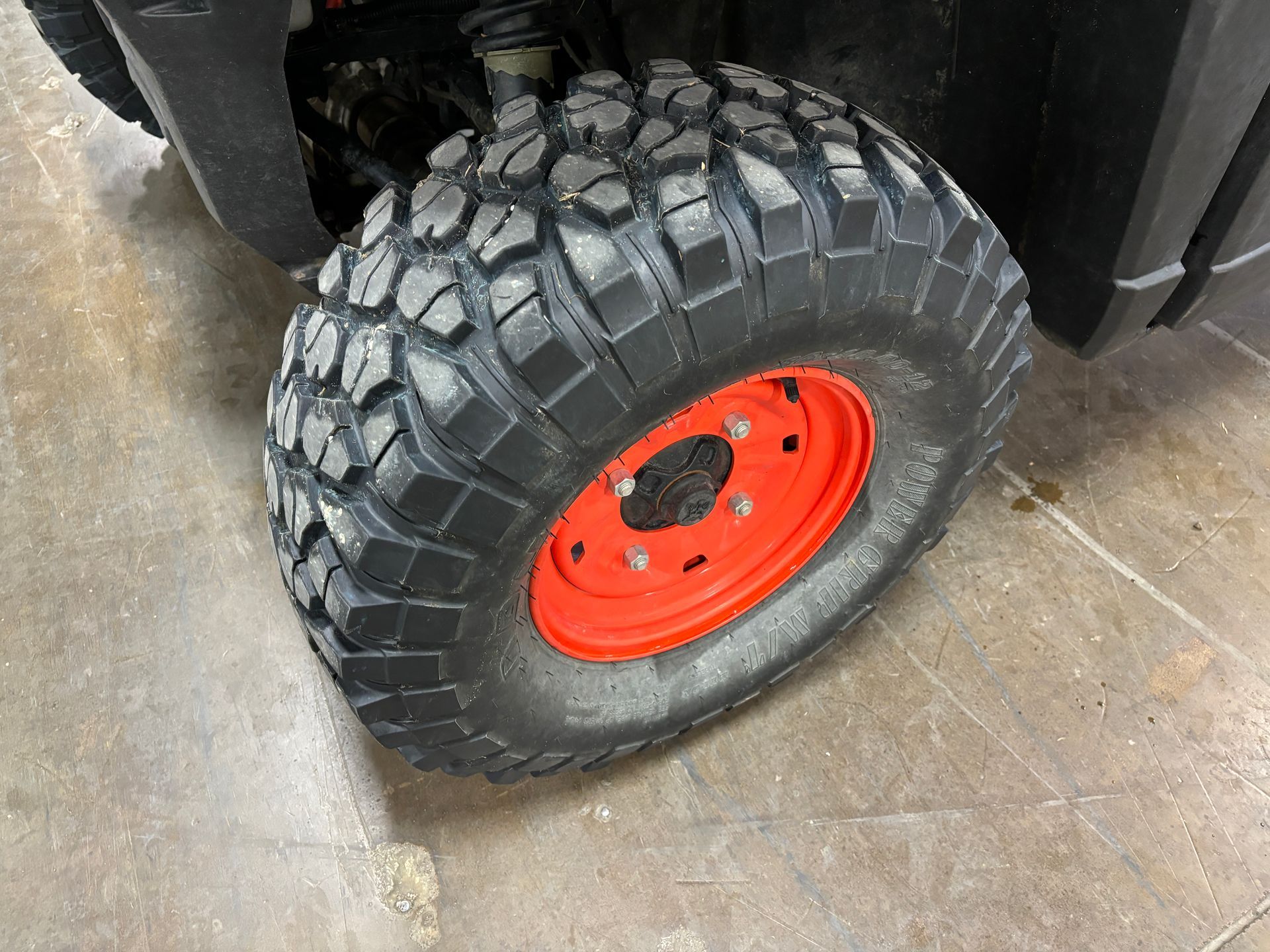 Black off-road tire on a vehicle, mounted on a red rim, on a concrete surface.