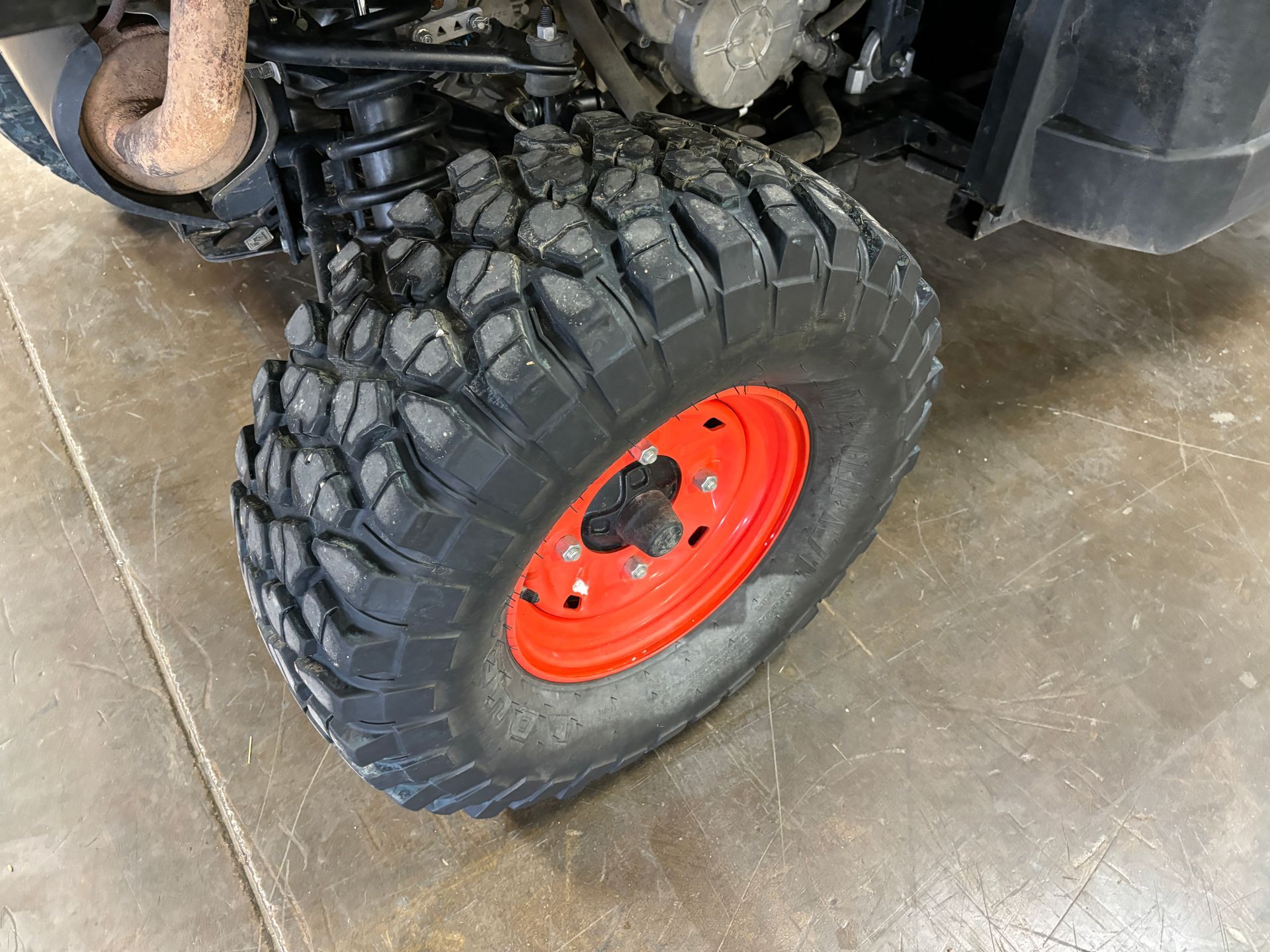 Black off-road tire on a vehicle with a red rim, set on a concrete surface.
