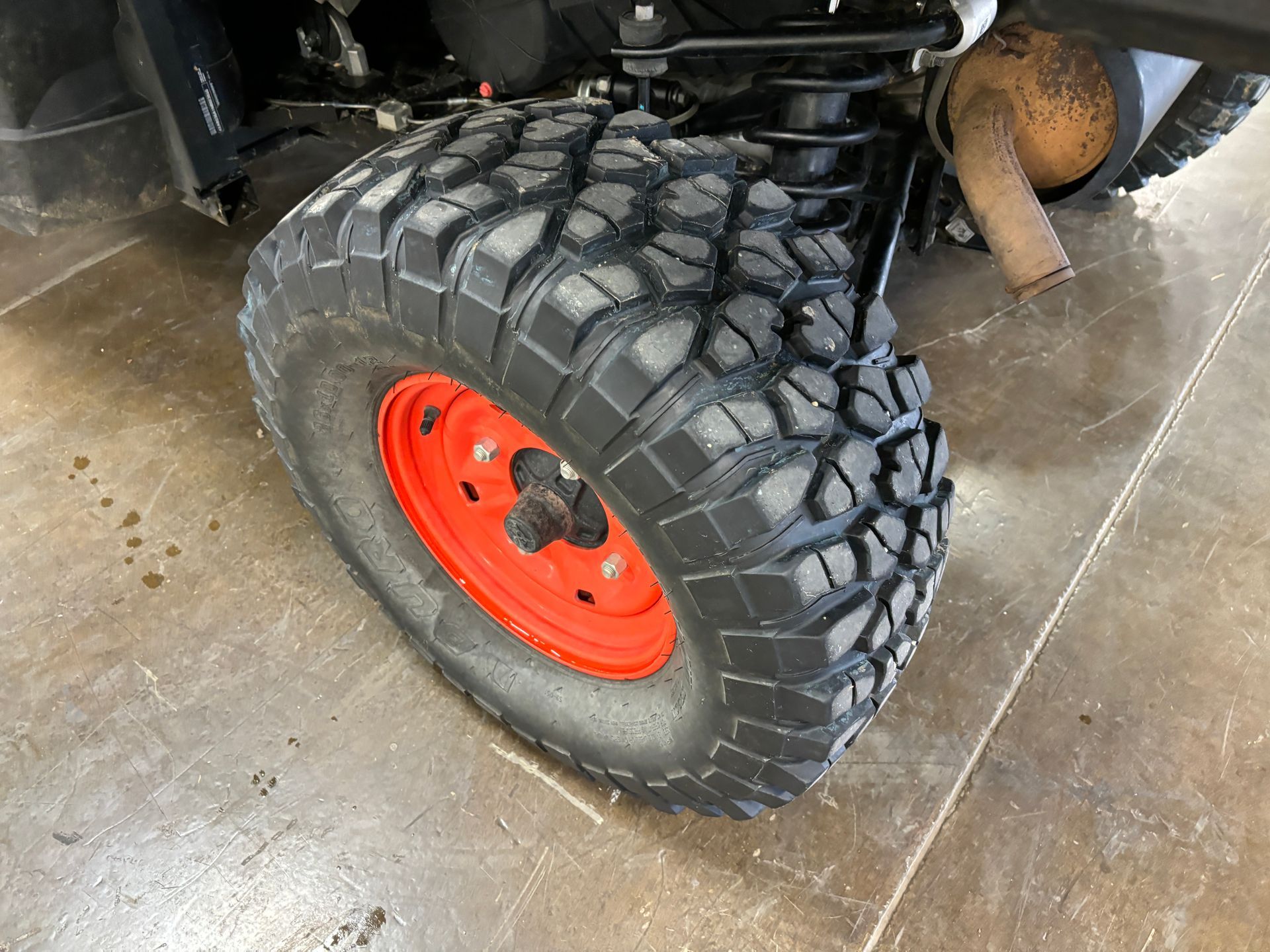 Black off-road tire on a vehicle with an orange wheel, on a concrete surface.