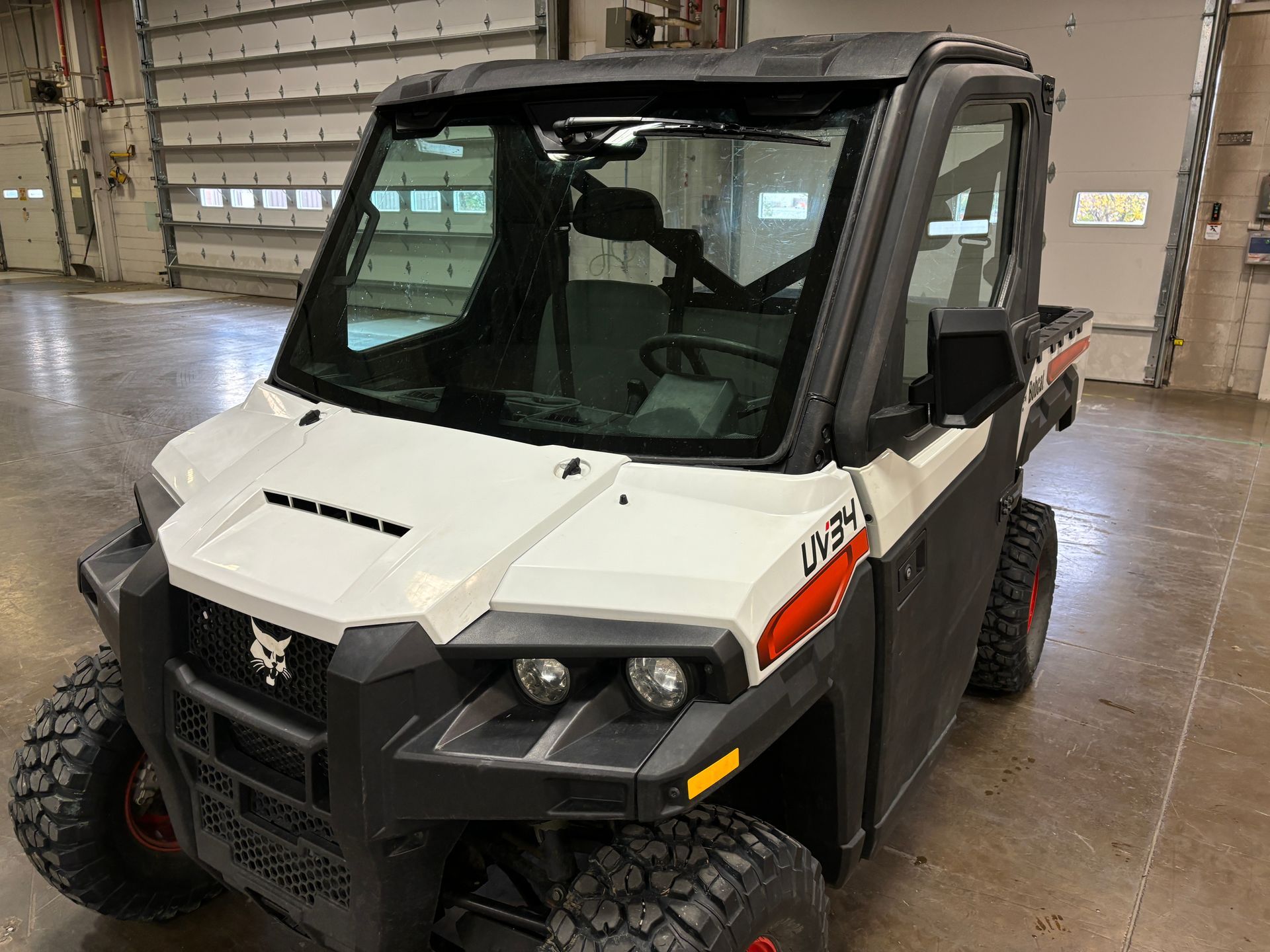 White and black Bobcat utility vehicle with windshield, in a garage.