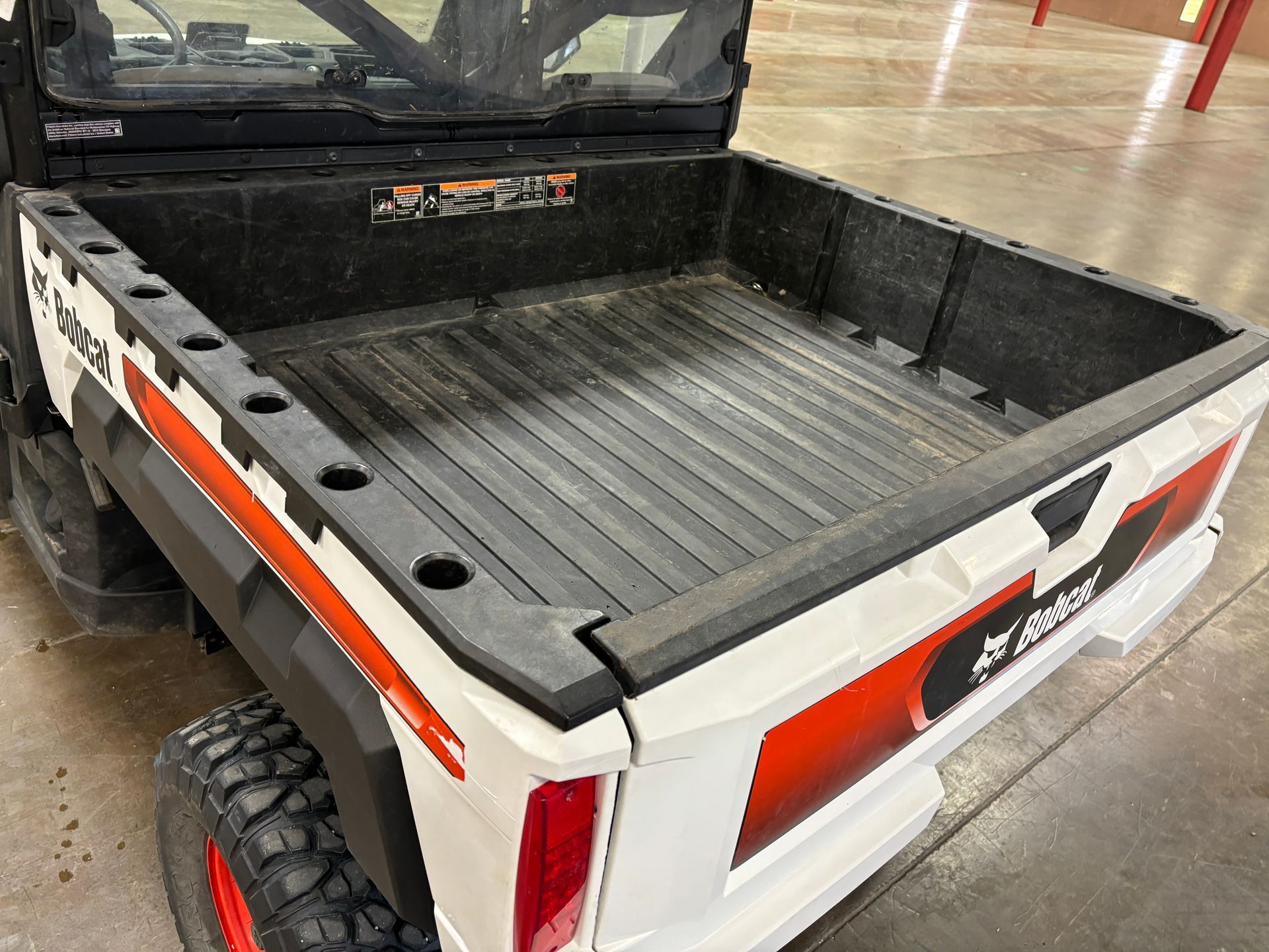 White Bobcat UTV bed with black textured floor and side panels, orange and white accents, and a large tire.