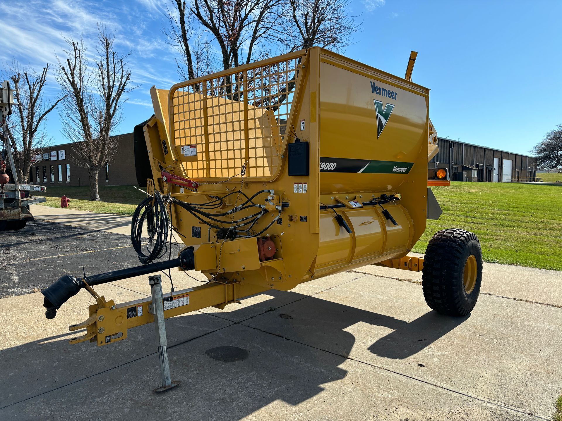 Yellow bale processor on a paved surface. Features a protective cage and a large mixing drum.