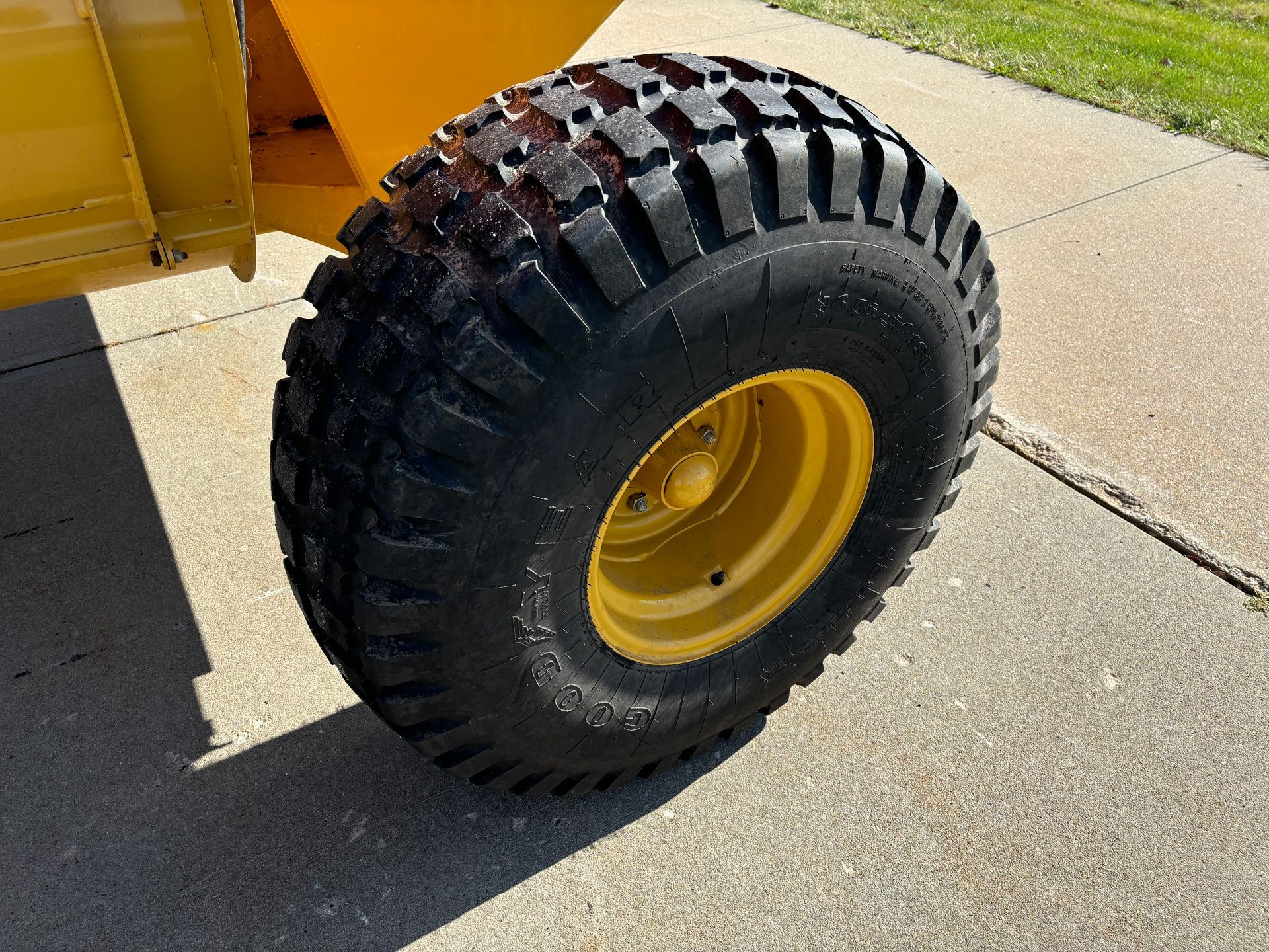 Yellow wheel of a machine with a thick black tread on a concrete surface.