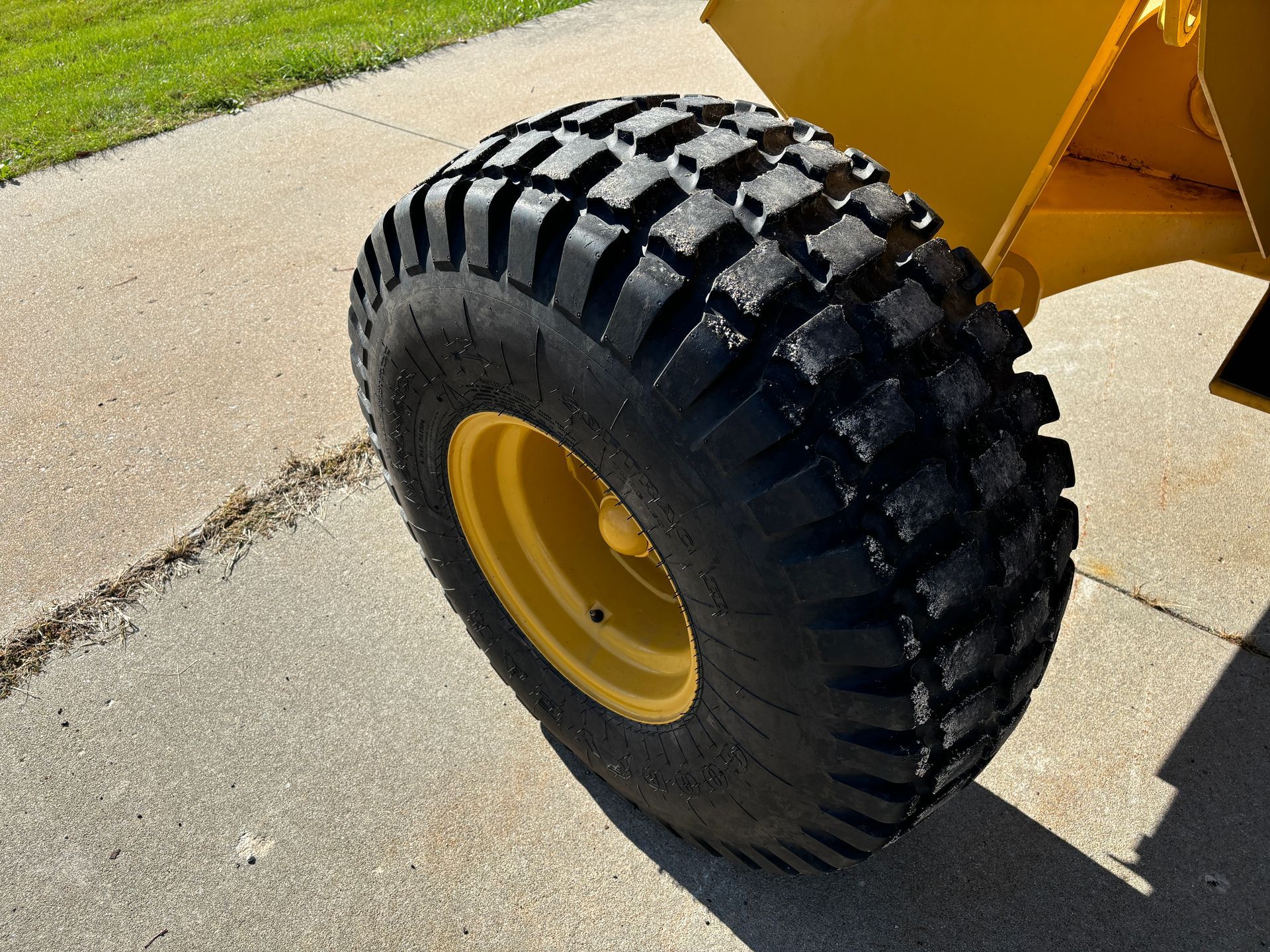 Yellow wheel of a machine with a thick black tread on a concrete surface.