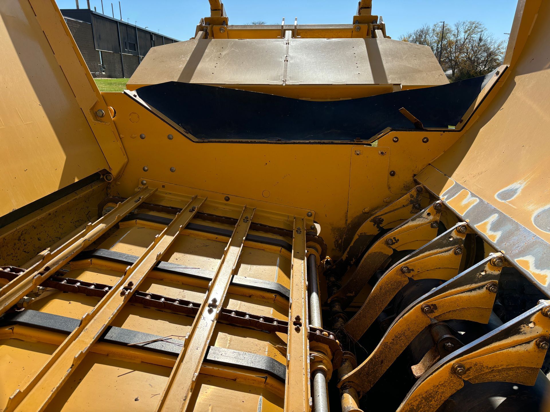 Yellow hay baler interior with rotating tines and conveyor, outdoors.