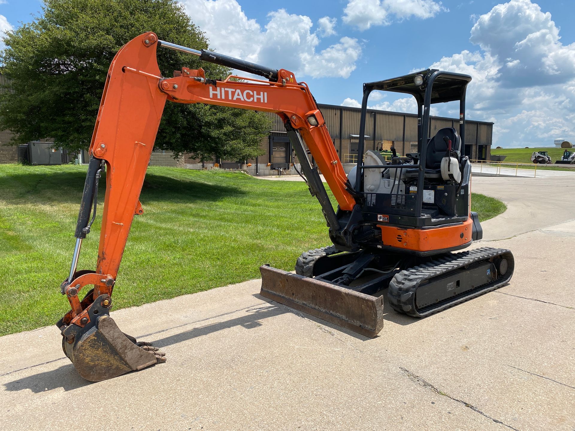 Orange and black Hitachi excavator parked on asphalt, with raised arm and bucket.