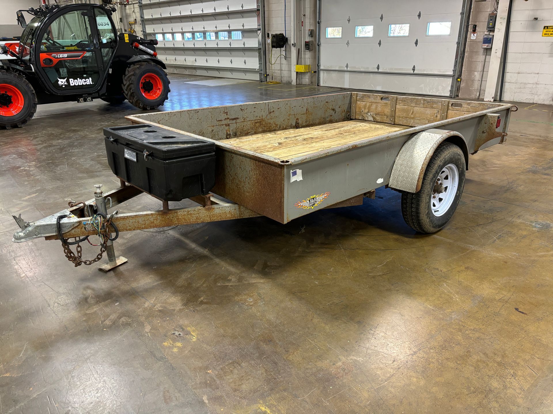 Gray utility trailer with a black toolbox, in an industrial setting.
