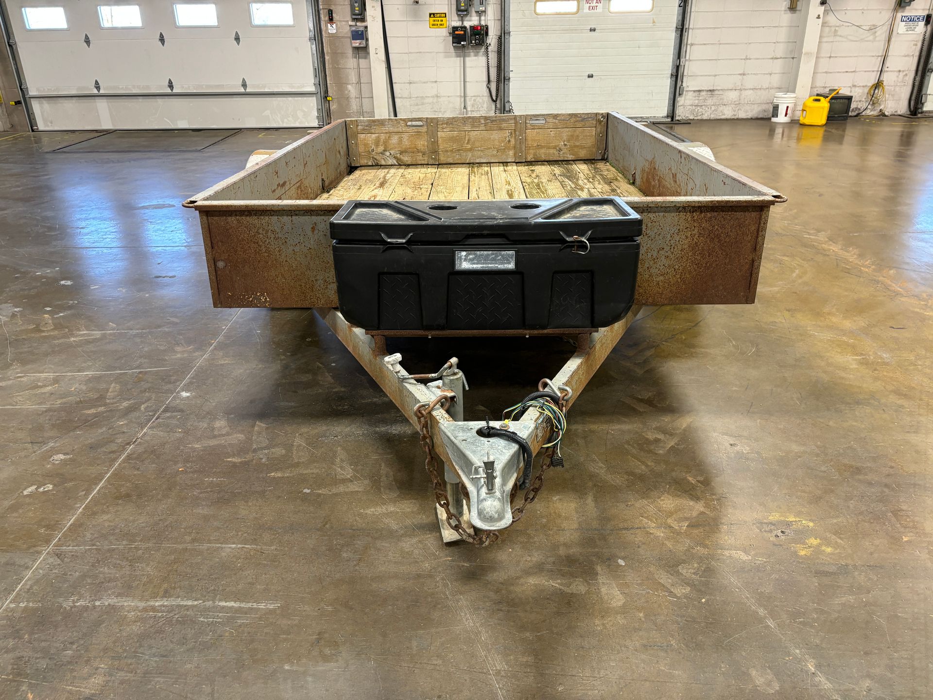 Utility trailer with rust, black storage box, and hitch. Indoors.